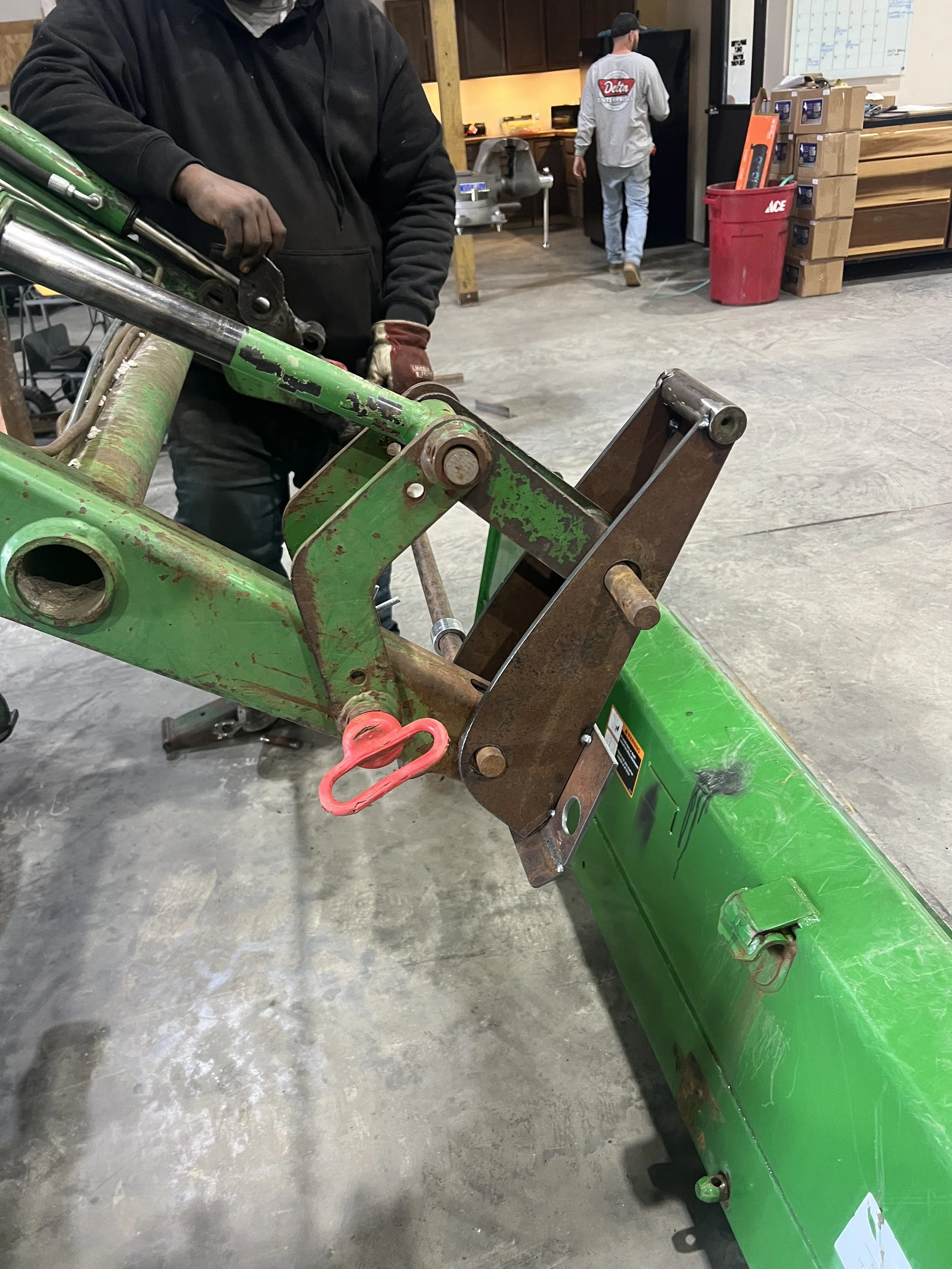 People working on a green tractor or piece of heavy machinery in a workshop or garage.