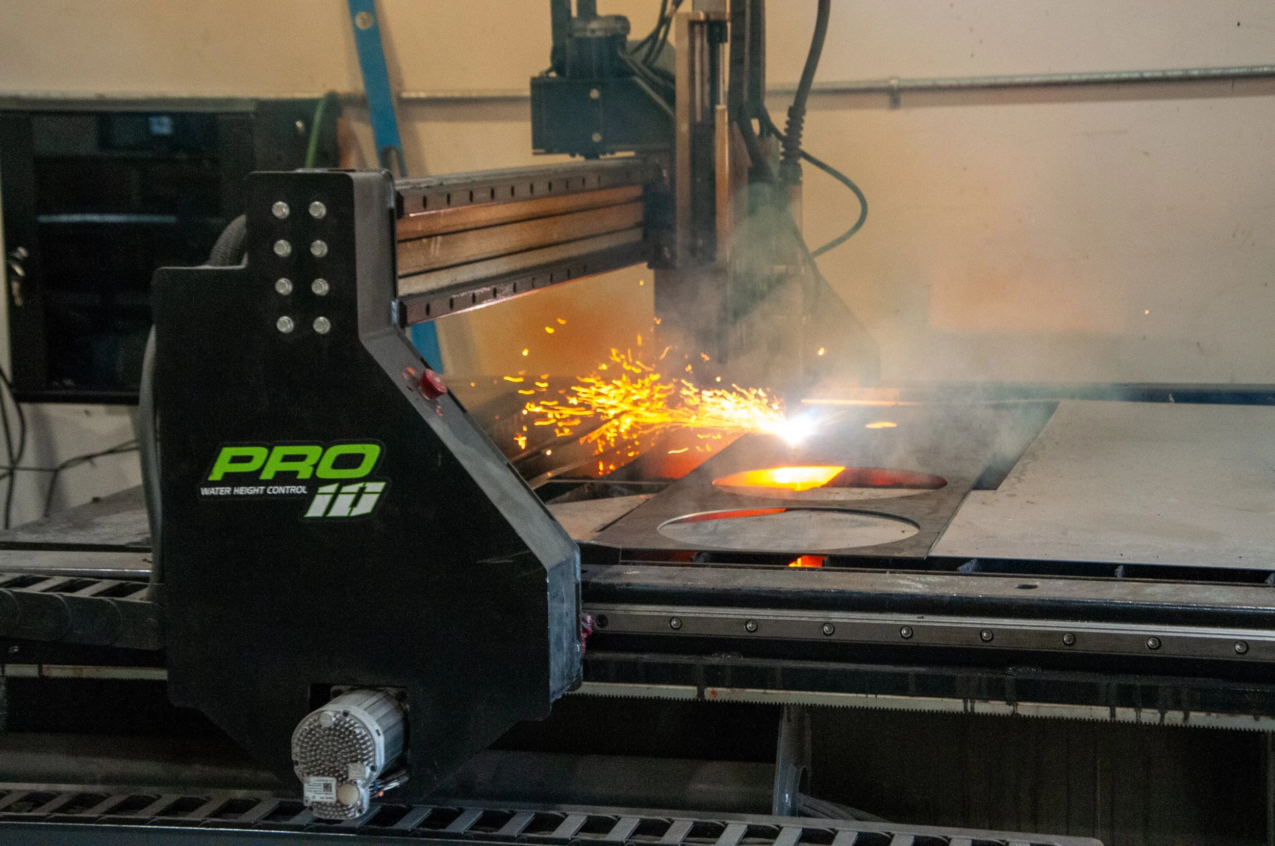 A CNC plasma cutter operating, with sparks flying as it cuts through metal sheets in a workshop.