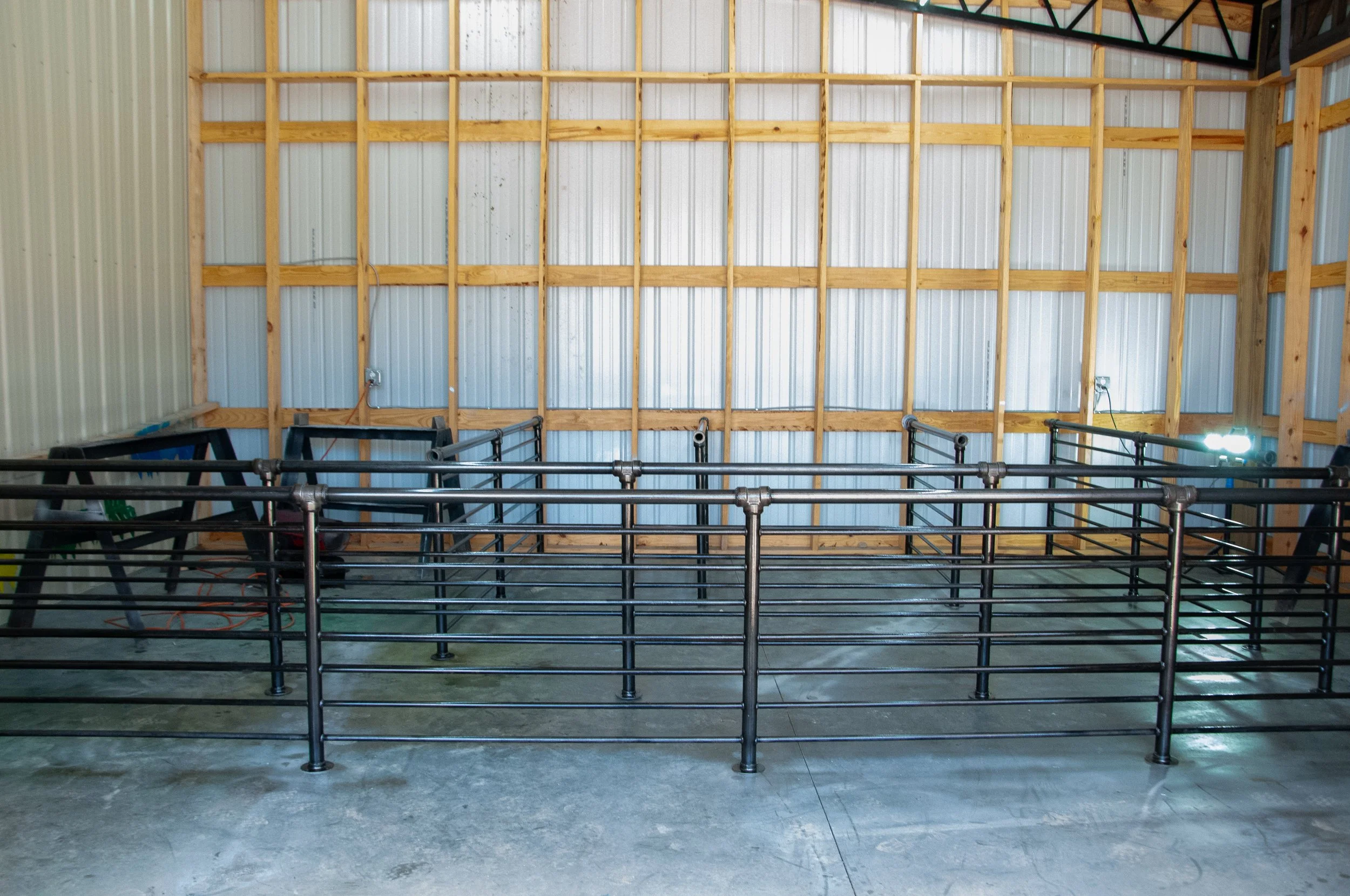 Empty indoor riding arena with metal fencing and unfinished wooden walls.