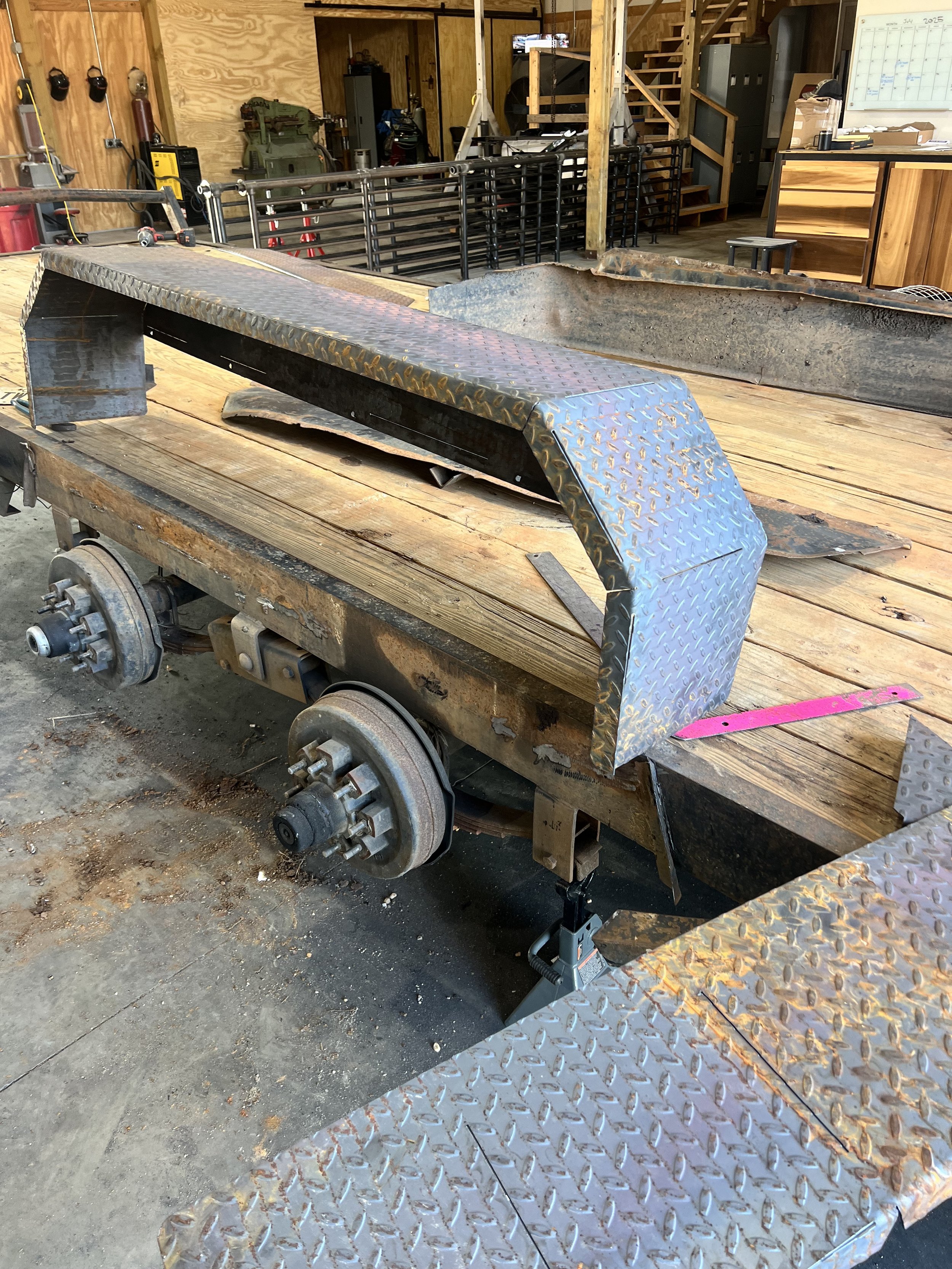 Metal used in vehicle construction with parts on a wooden worktable in a garage workshop.