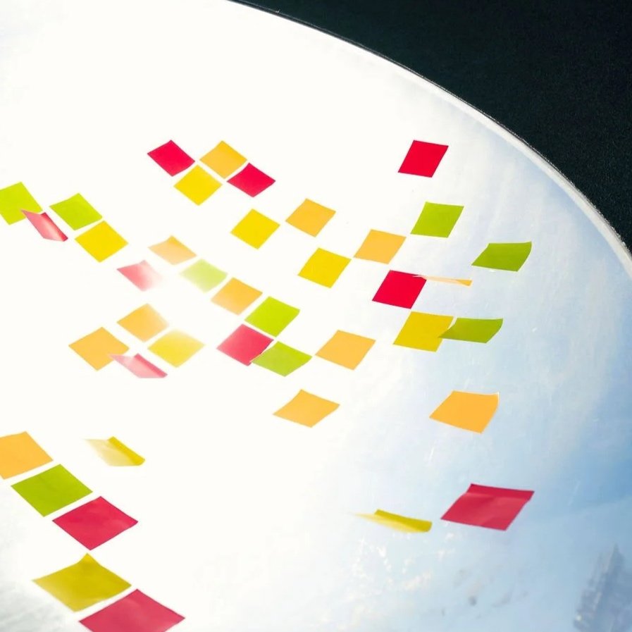 Bunte Klebezettel in Rot, Gelb, Orange und Grün auf einer weißen Oberfläche, verteilt in einer diagonalen Anordnung.