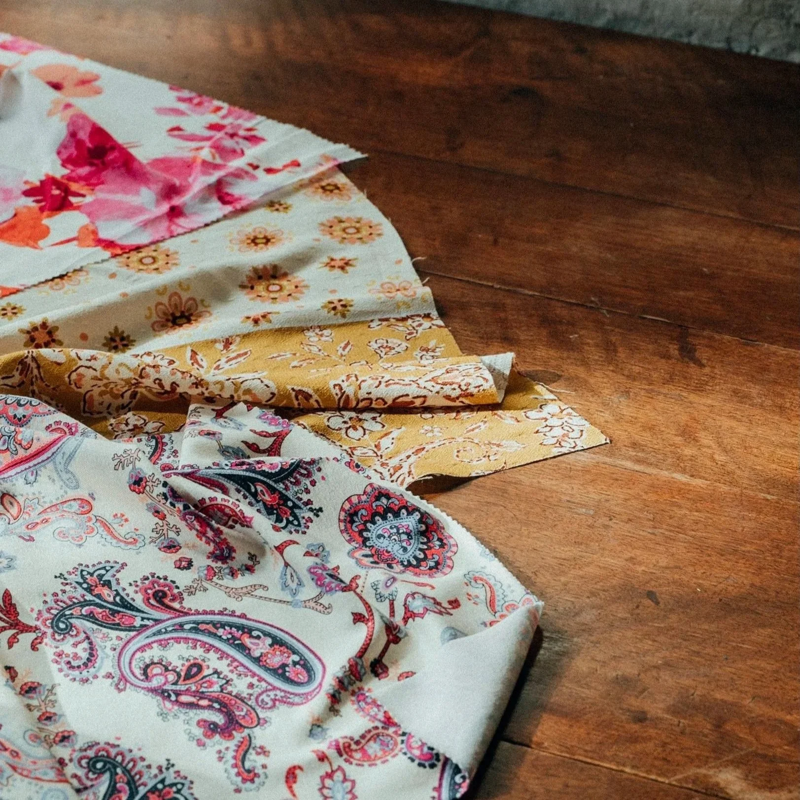 Festons de tissus colorés avec des motifs floraux et de motifs paisley, posés sur une table en bois.