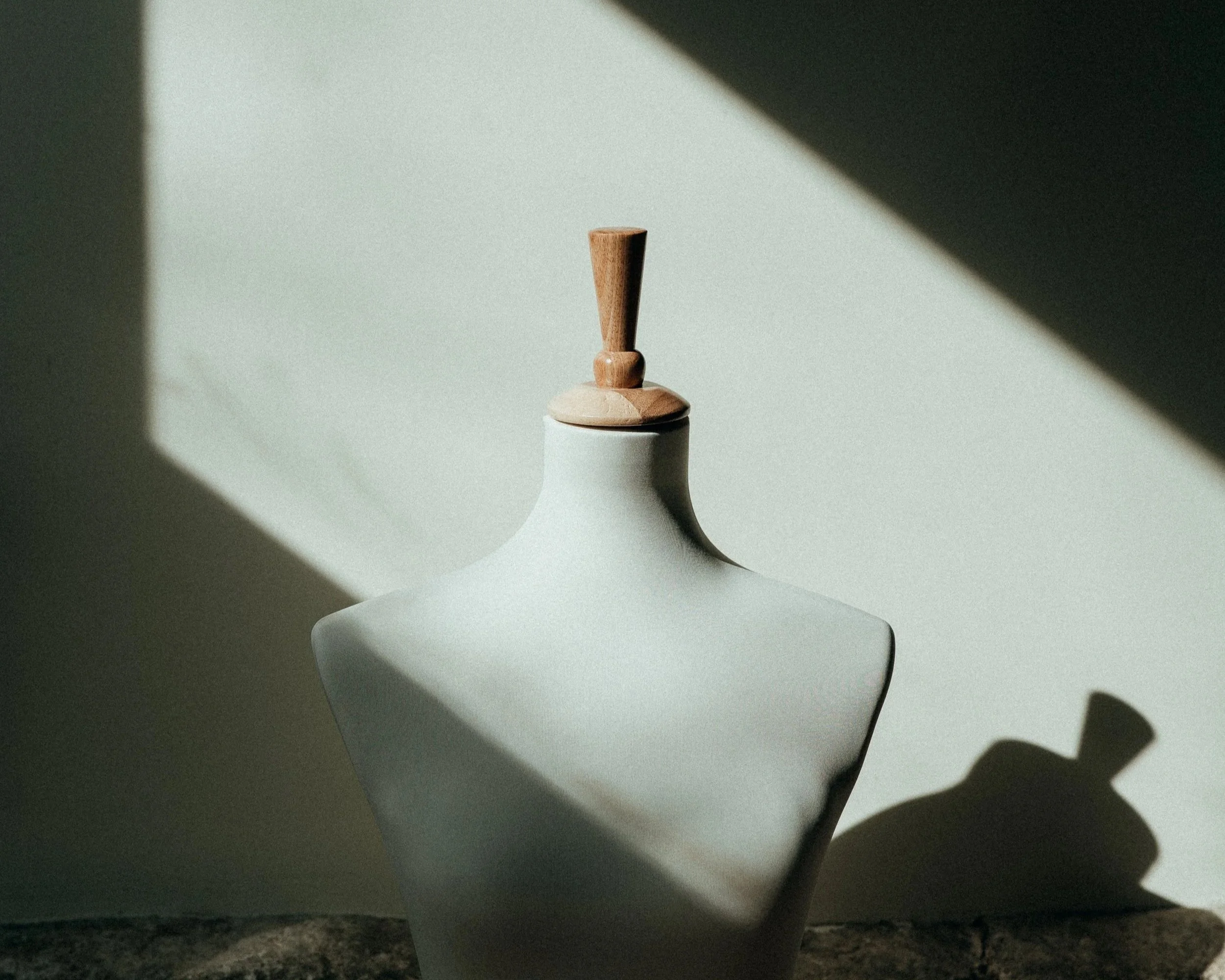 Vase blanc avec un bouchon en bois, éclairé par la lumière naturelle créant des ombres.