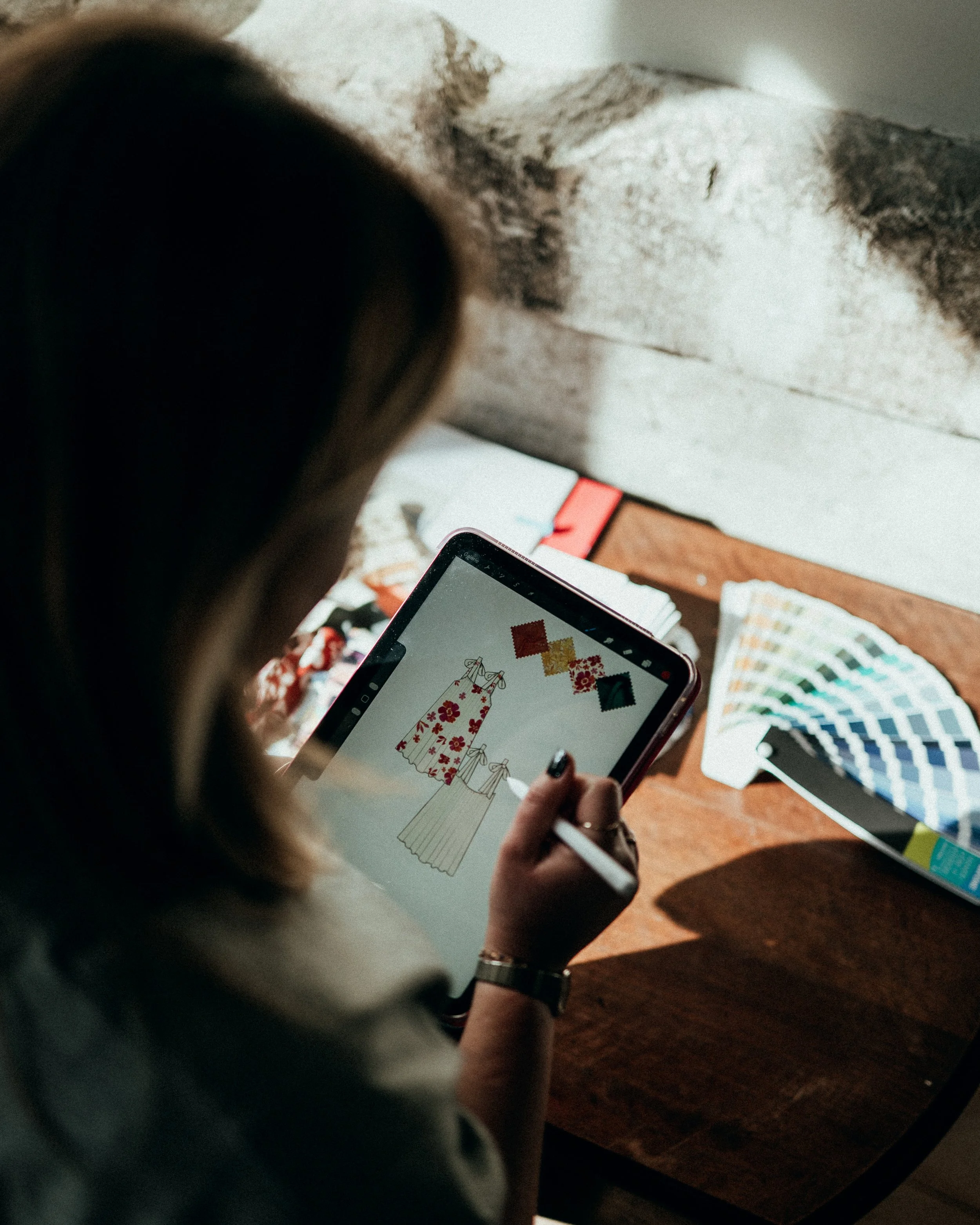 Une personne regarde une tablette avec un dessin de robes et des échantillons de tissus à côté.