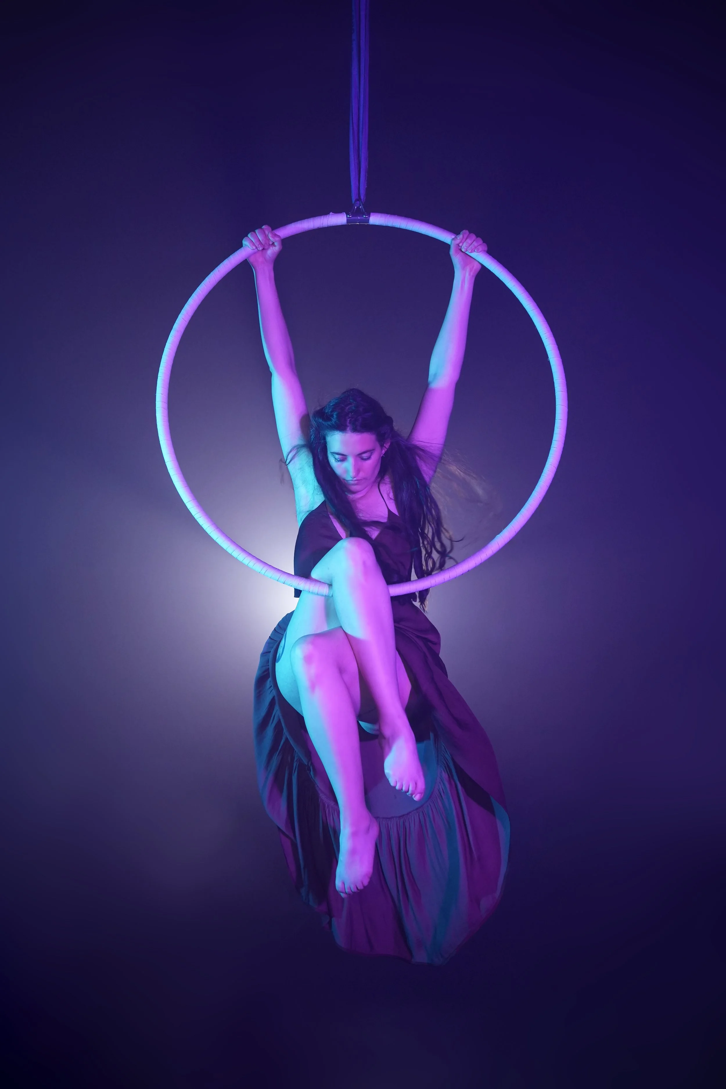 Une femme effectue une performance d'acrobatie dans un cercle aérien suspendu avec un éclairage violet et bleu