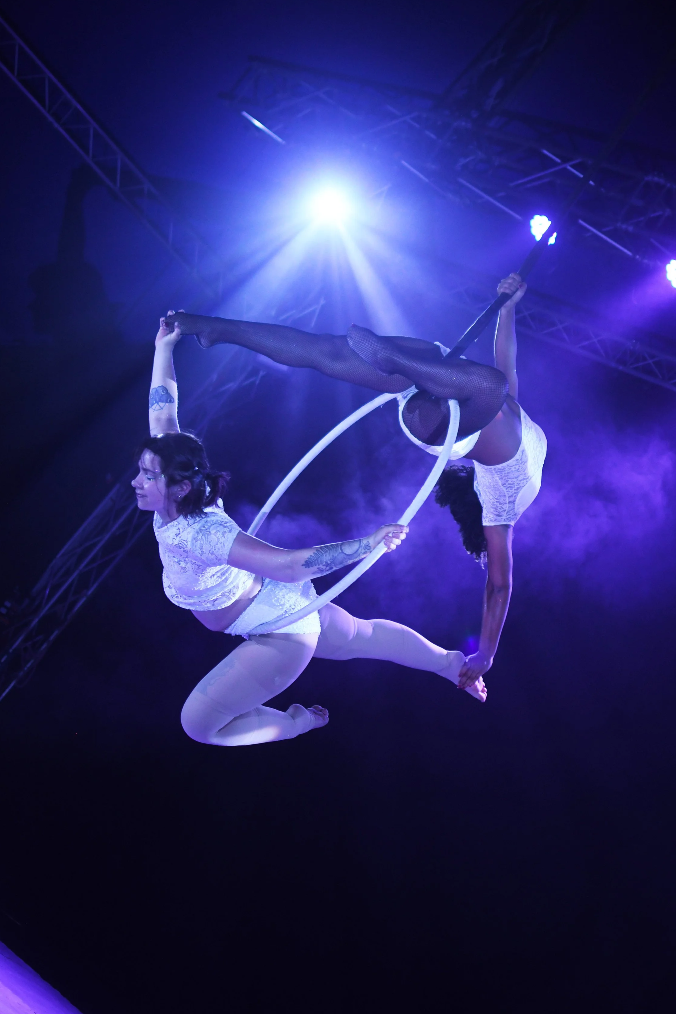 Deux artistes acrobates réalisant une performance aérienne en plumes blanches, sous un éclairage violet et bleu dans une scène de spectacle.