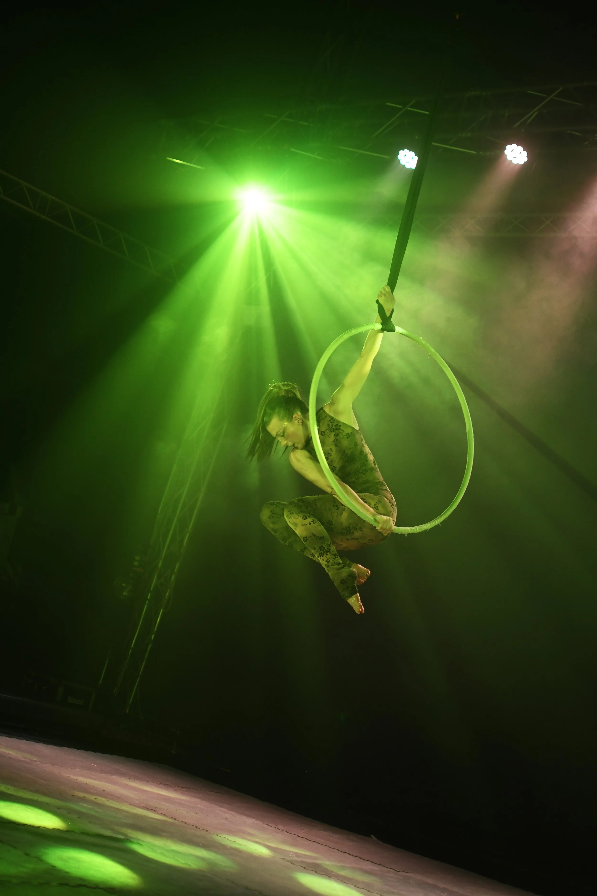 Une artiste de cirque effectue un numéro suspendu dans un cerceau en utilisant un tissu lors d'un spectacle sous un éclairage vert.
