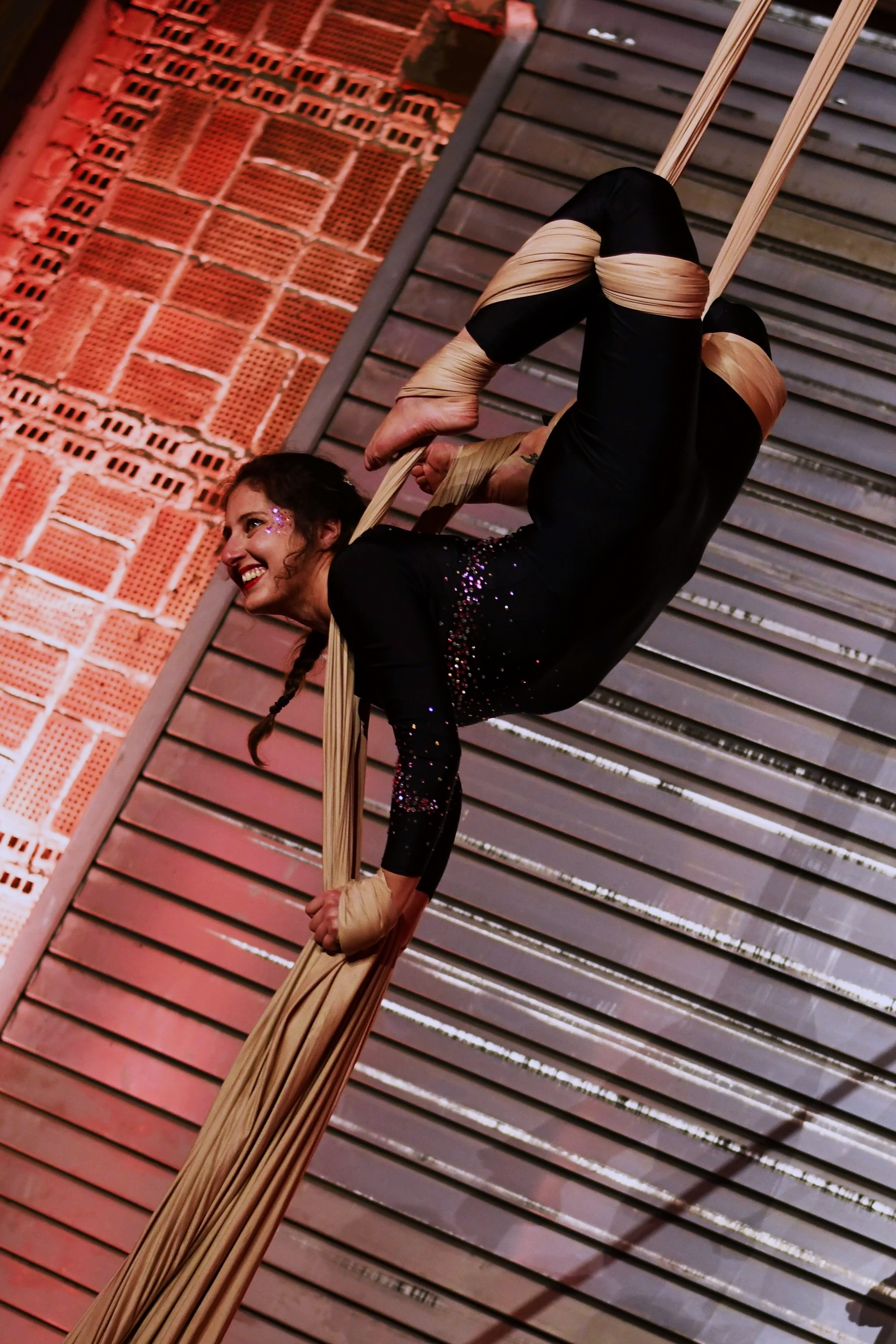 Une femme effectue une performance d'acrobatie aérienne avec des bandes de tissu beige suspendues au plafond, dans un environnement industriel.