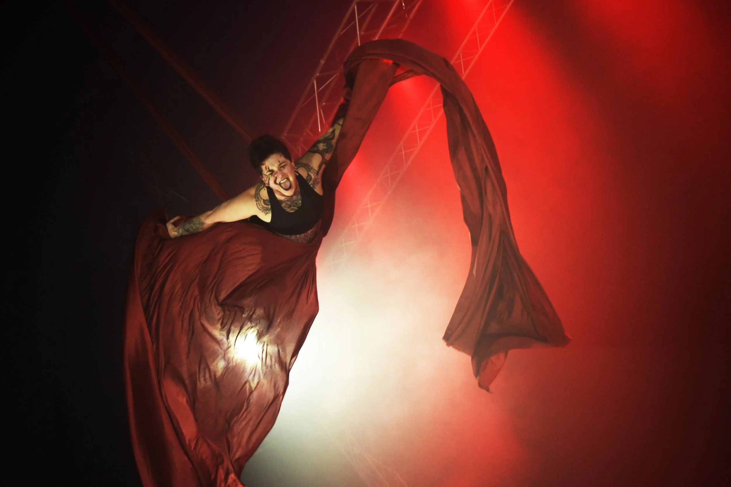 Une artiste acrobate effectue une performance aérienne lors d'un spectacle, suspendue à des tissus rouges avec un éclairage chaud et rouge dans une scène de scène.