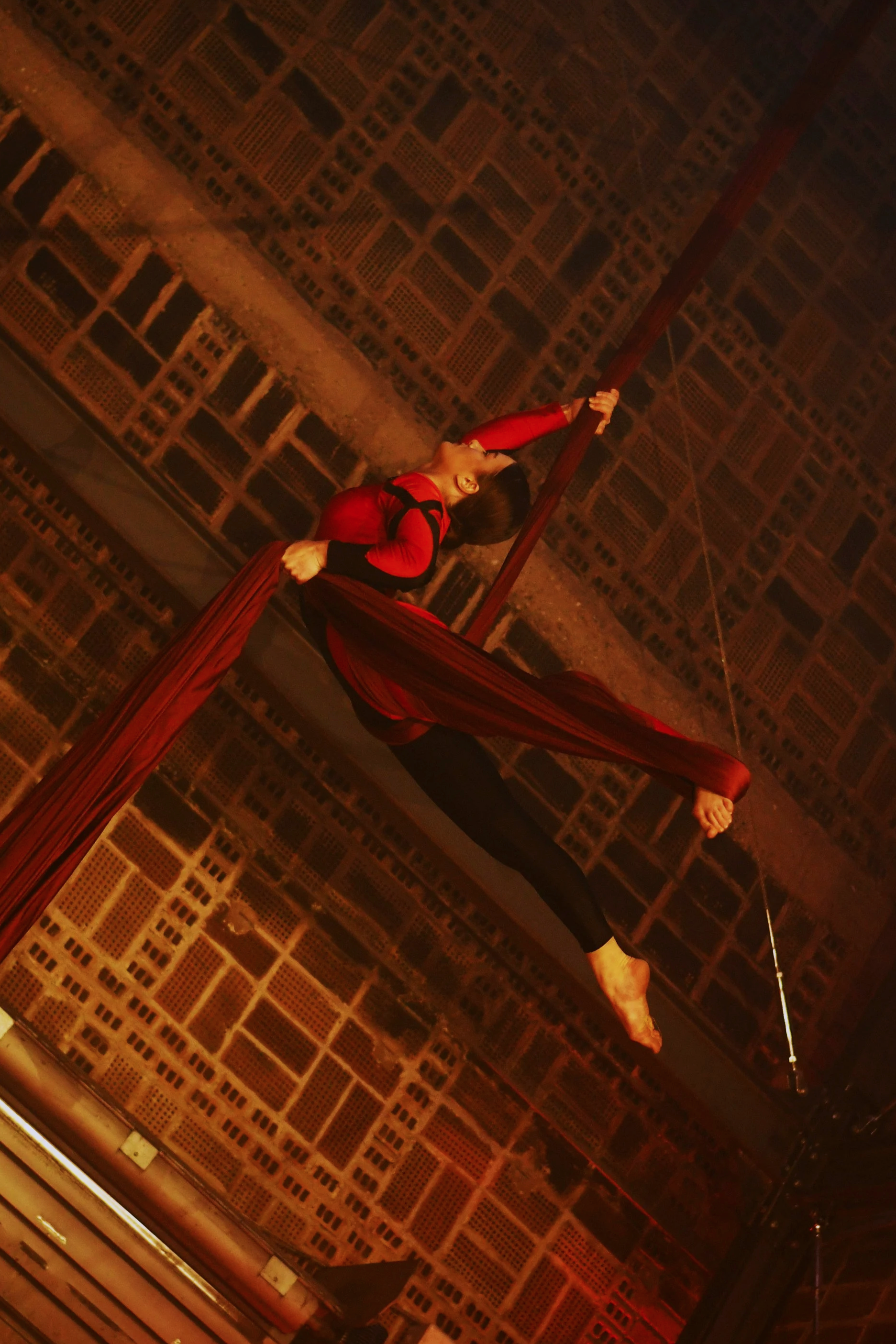 Une artiste de cirque en costume rouge effectue une performance aérienne avec des tissus rouges suspendus au plafond.