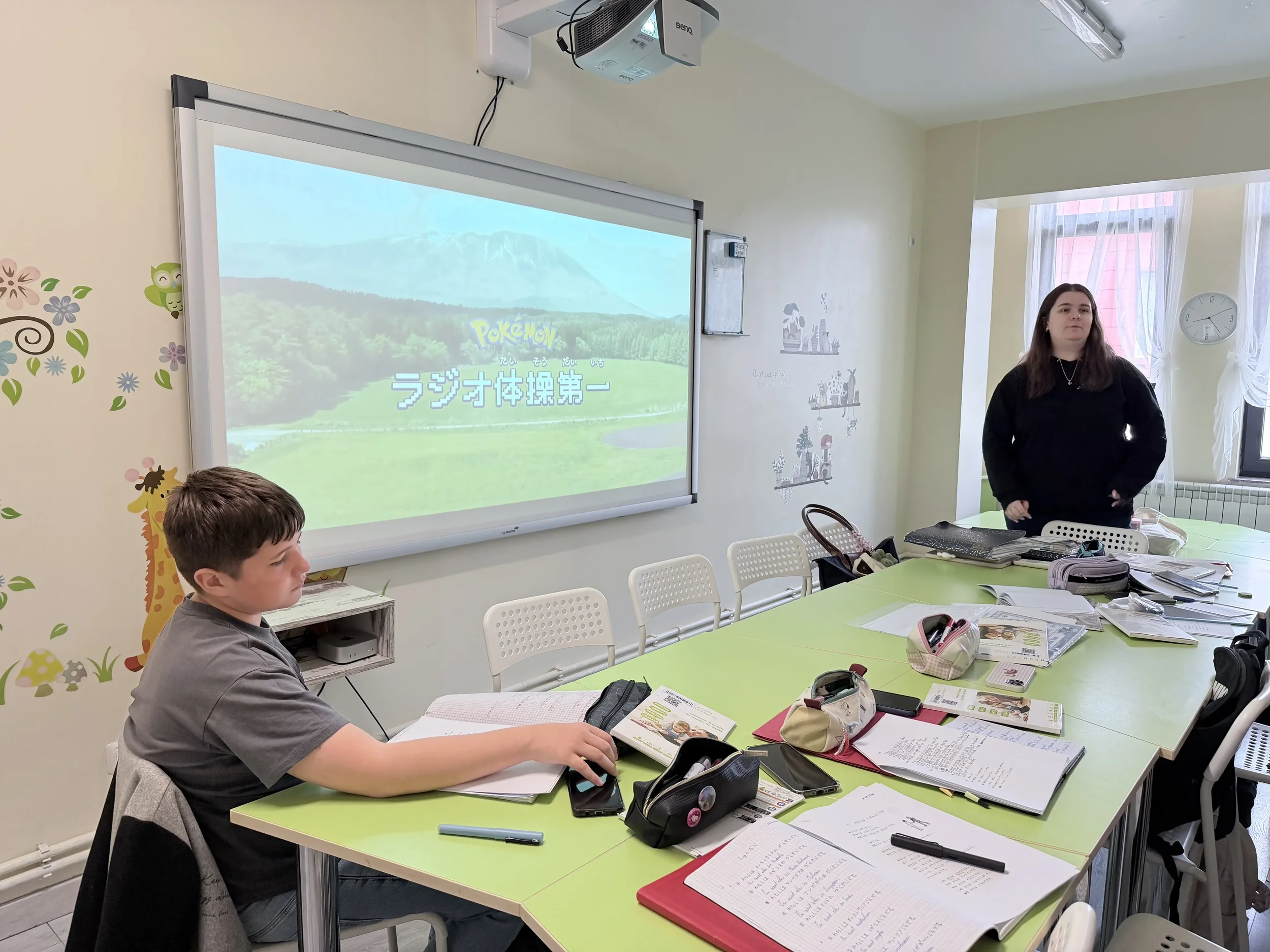 Un elev studiind la masă în timp ce profesoara prezintă o lecție interactivă pe ecranul digital mare din sala de curs de japonezǎ la York Rose in Constanta