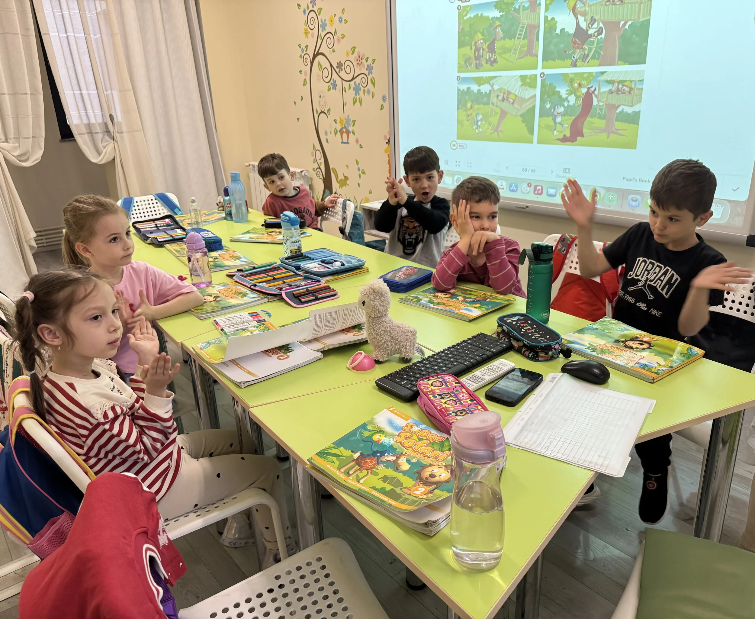 Grup de copii preșcolari participând la un curs de limba engleză la York Rose Language School în Constanța. Copiii folosesc manuale colorate și o tablă interactivă într-o sală de clasă luminoasă.
