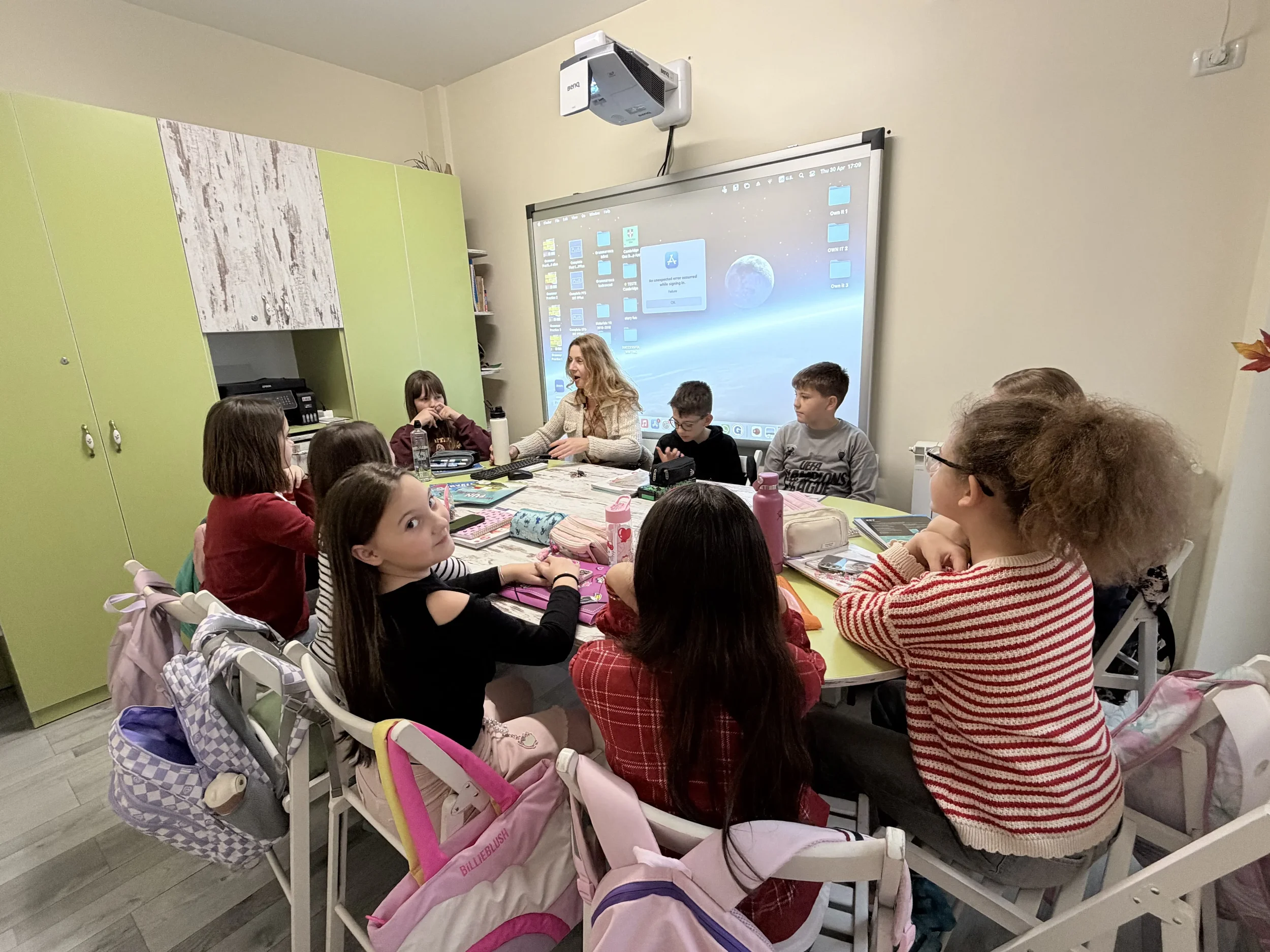 Atmosferă caldă în timpul orelor de curs la York Rose Language School, cu o profesoară ghidând o discuție interactivă la masa de studiu cu un grup de copii.