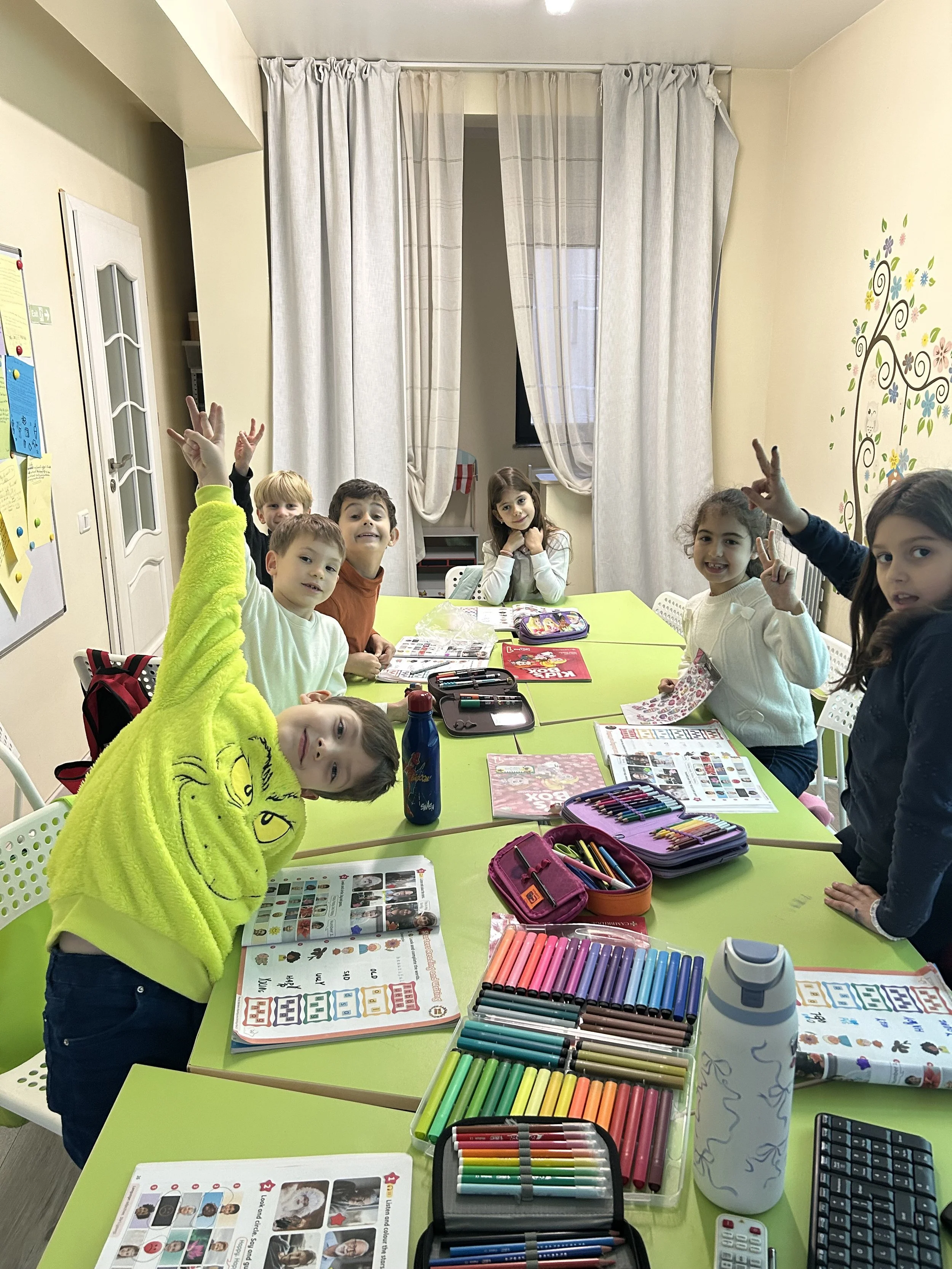 Copii participând la o activitate interactivă de învățare a limbii engleze la York Rose Language School din Constanța, lucrând împreună la o masă cu materiale educaționale și culori.