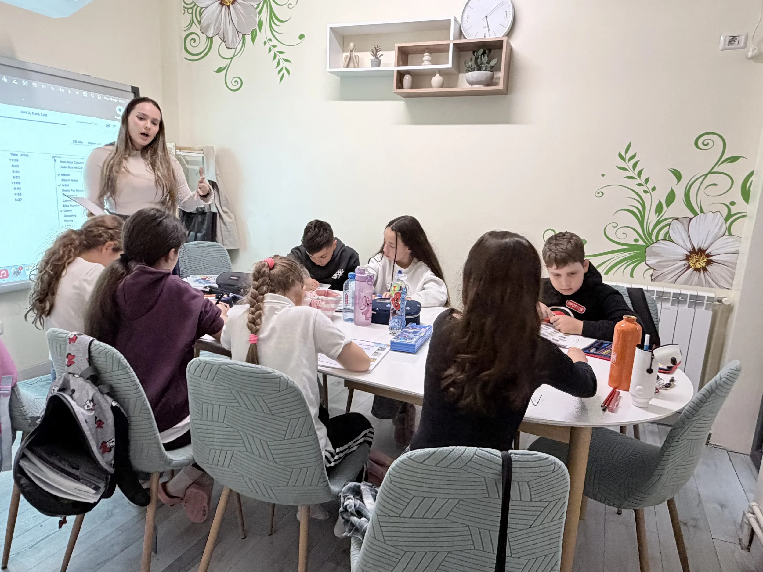 Grup de copii scriind în manuale la o masă albă rotundă în timpul orelor moderne de limba germană la York Rose Constanța