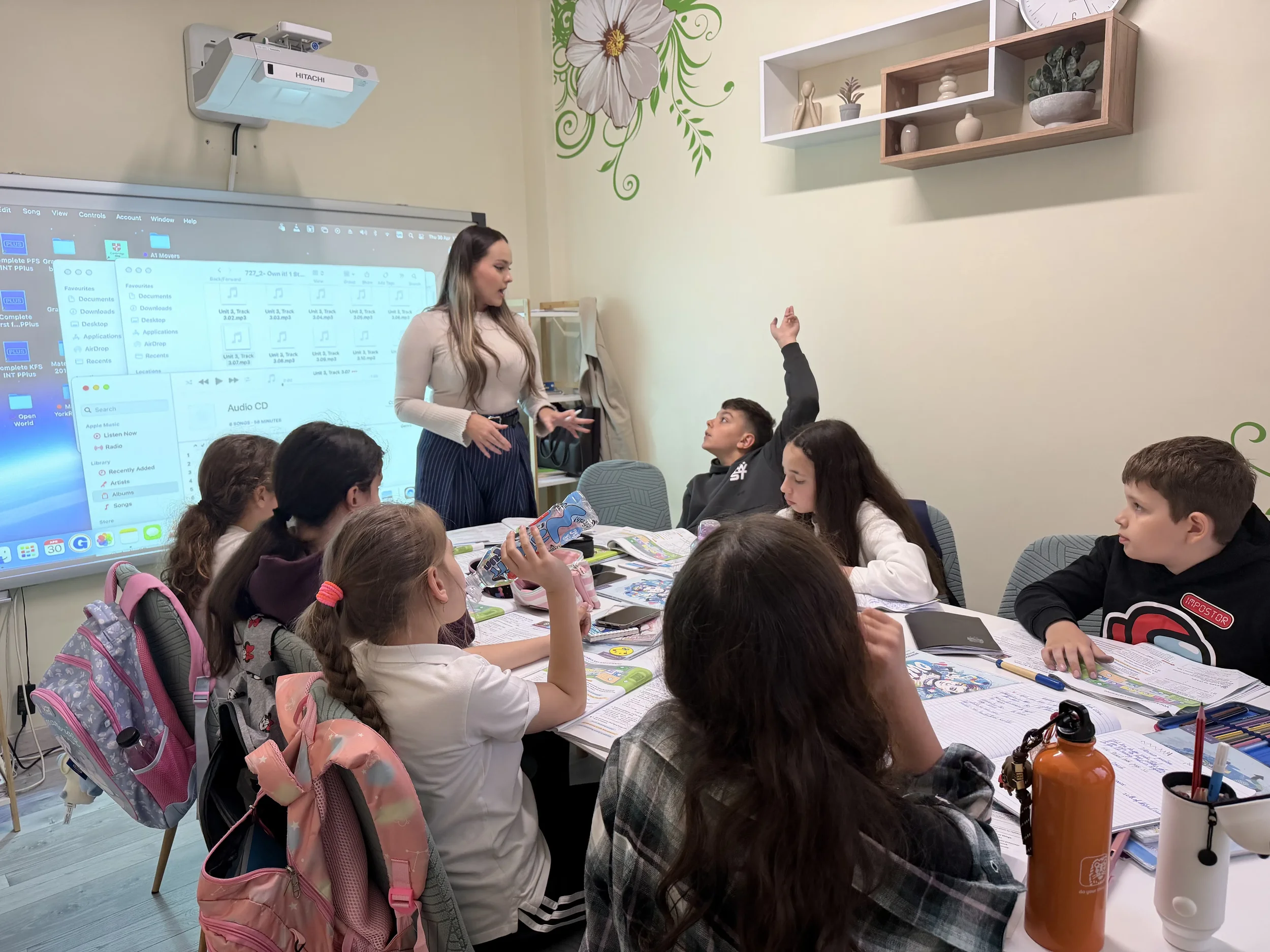 Profesoară de germanǎ la York Rose Constanțaexplicând o lecție la ecranul digital în fața unor elevi atenți, un băiat ridicând mâna pentru a răspunde.