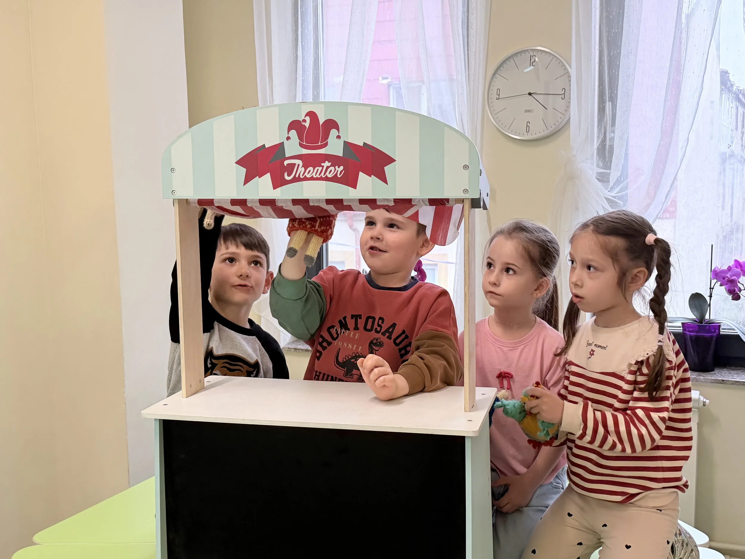 Patru copii folosind un teatru de păpuși din lemn inscripționat 'Theater' pentru exerciții de storytelling și conversație în limba engleză la școala York Rose