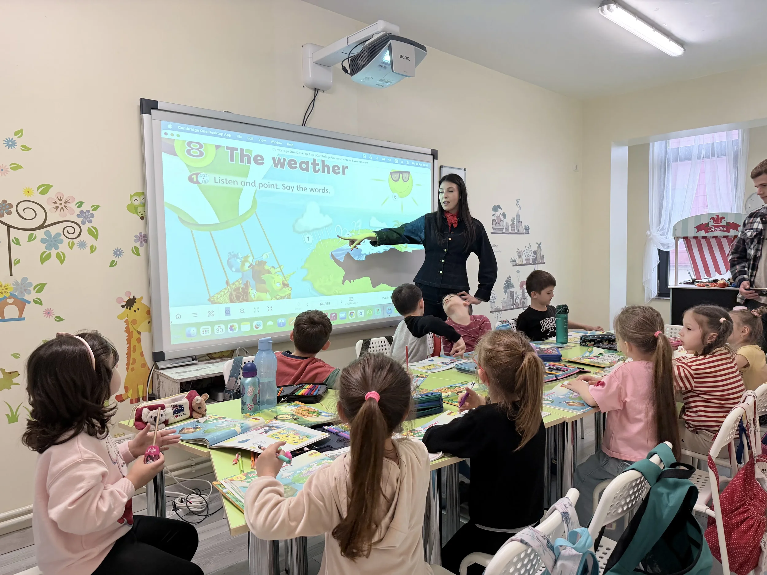Profesoară explicând lecția despre vreme la engleza, pe ecranul digital în fața unei clase de copii la York Rose Constanța
