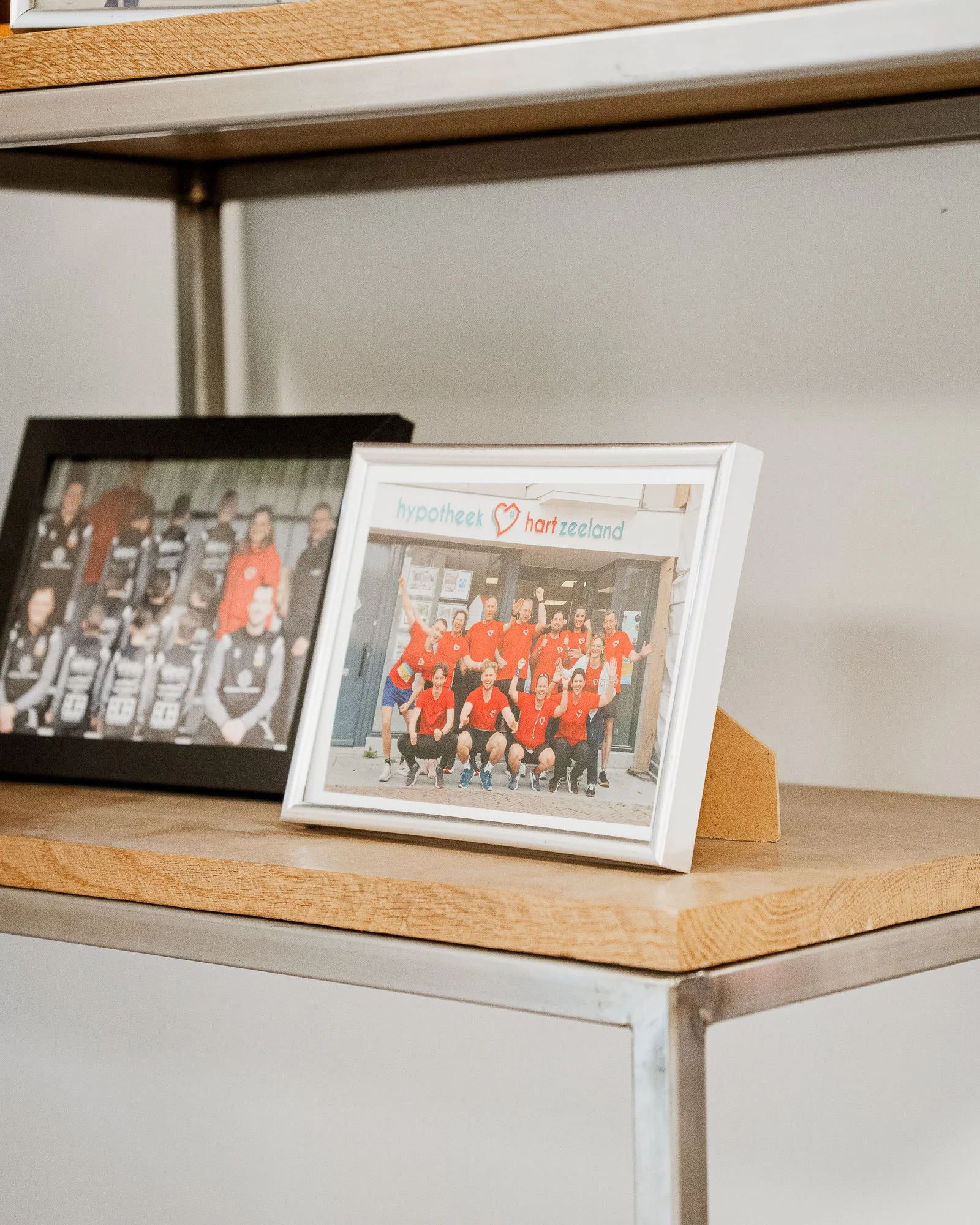 Twee fotolijsten met foto's, een op een houten tafel, met een bord met de tekst 'hypotheek hart zeeland' in de achtergrond.