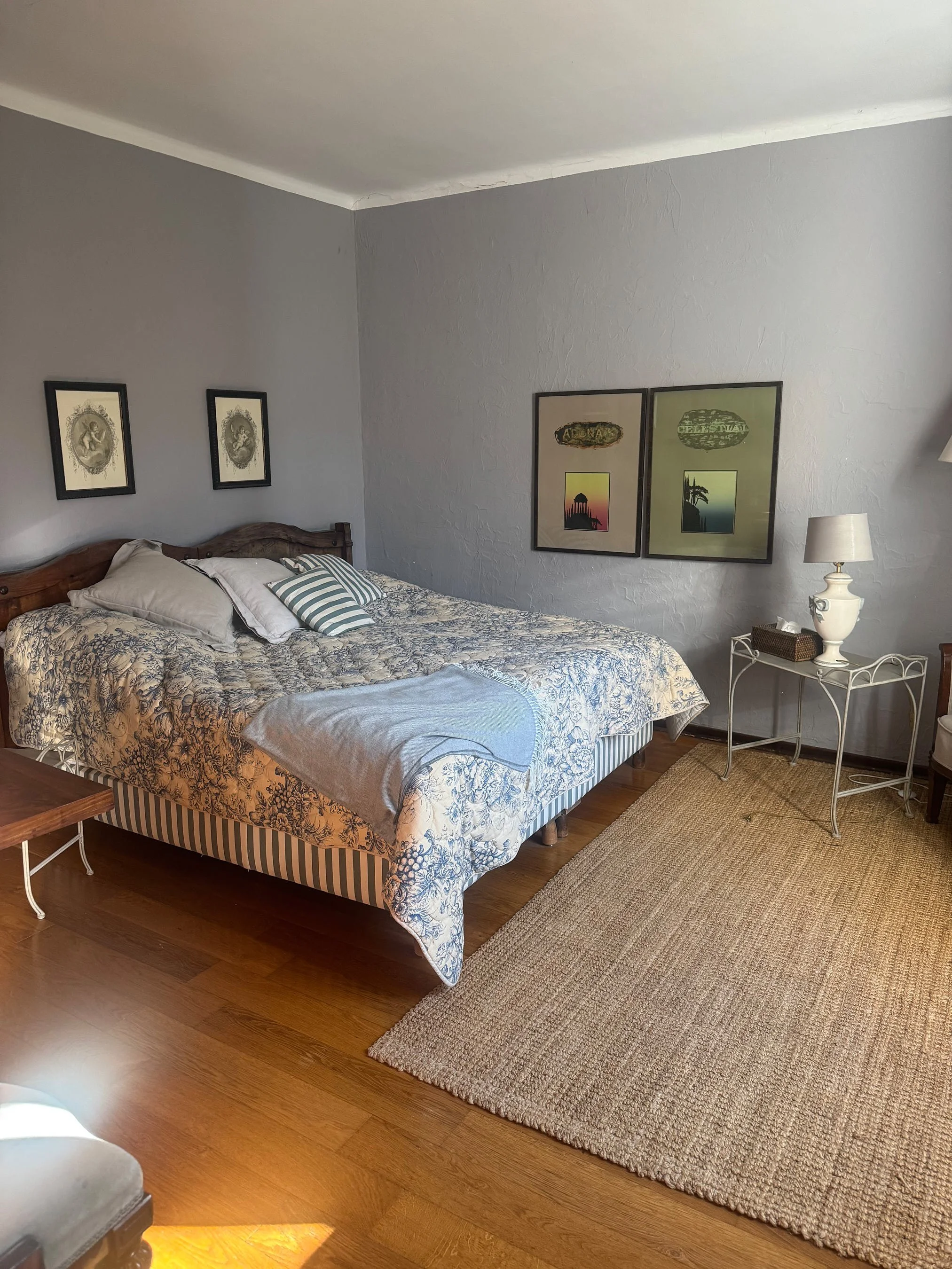 Schlafzimmer mit Ehebett, Nachttisch mit Lampe, Teppich auf Holzboden, drei Wandbilder, und Garderobe