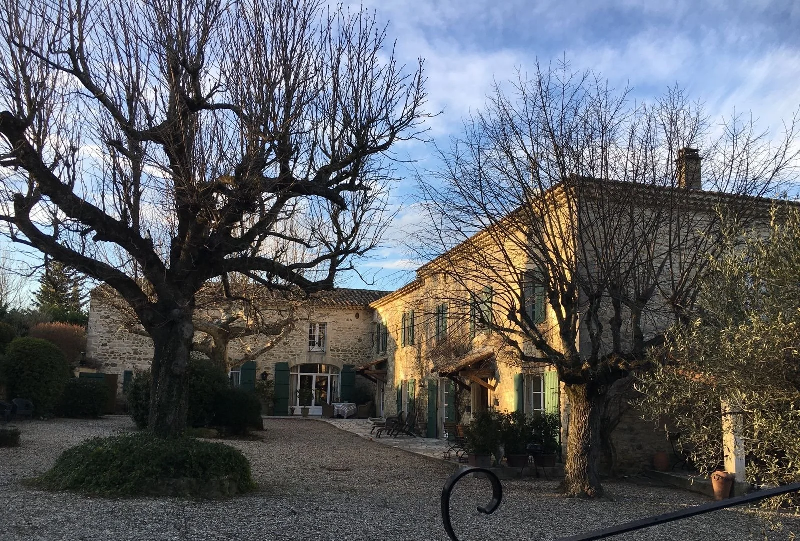Ein idyllisches Landhaus mit Steinfassade, umgeben von Bäumen ohne Blätter, bei Sonnenuntergang, mit einer Terrasse und Gartenmöbeln.