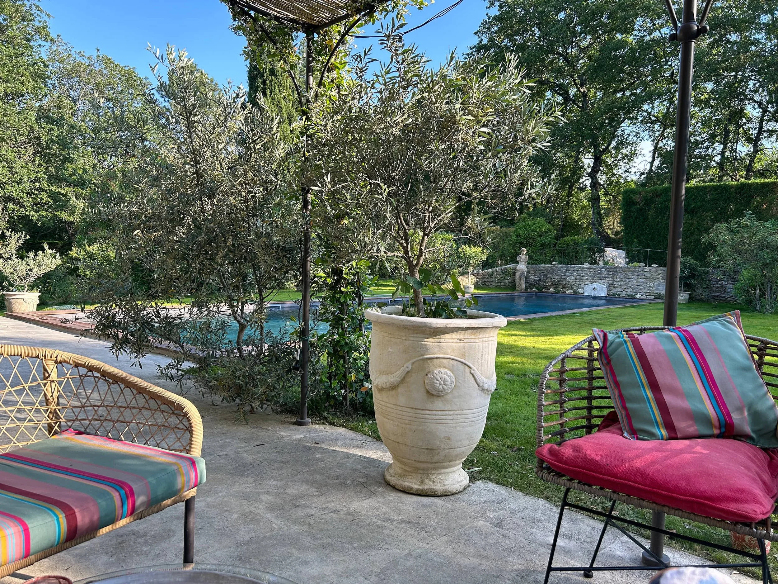 Garten mit Pool, mediterranen Pflanzen, Steinskulptur, Sitzgelegenheiten mit bunten Kissen.