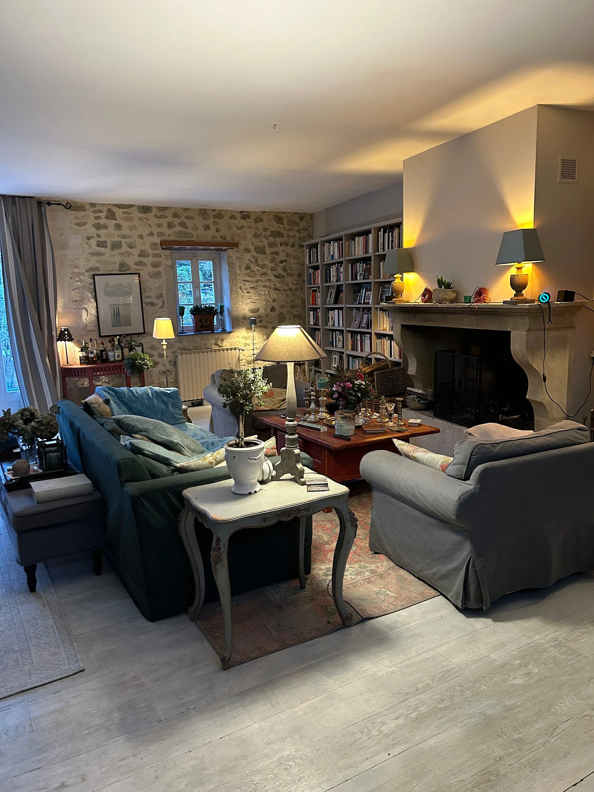 Gemütliches Wohnzimmer mit Steinwand, Bücherregal, Kamin und bequemen Sofas, mit verschiedenen Lampen und Dekorationen.