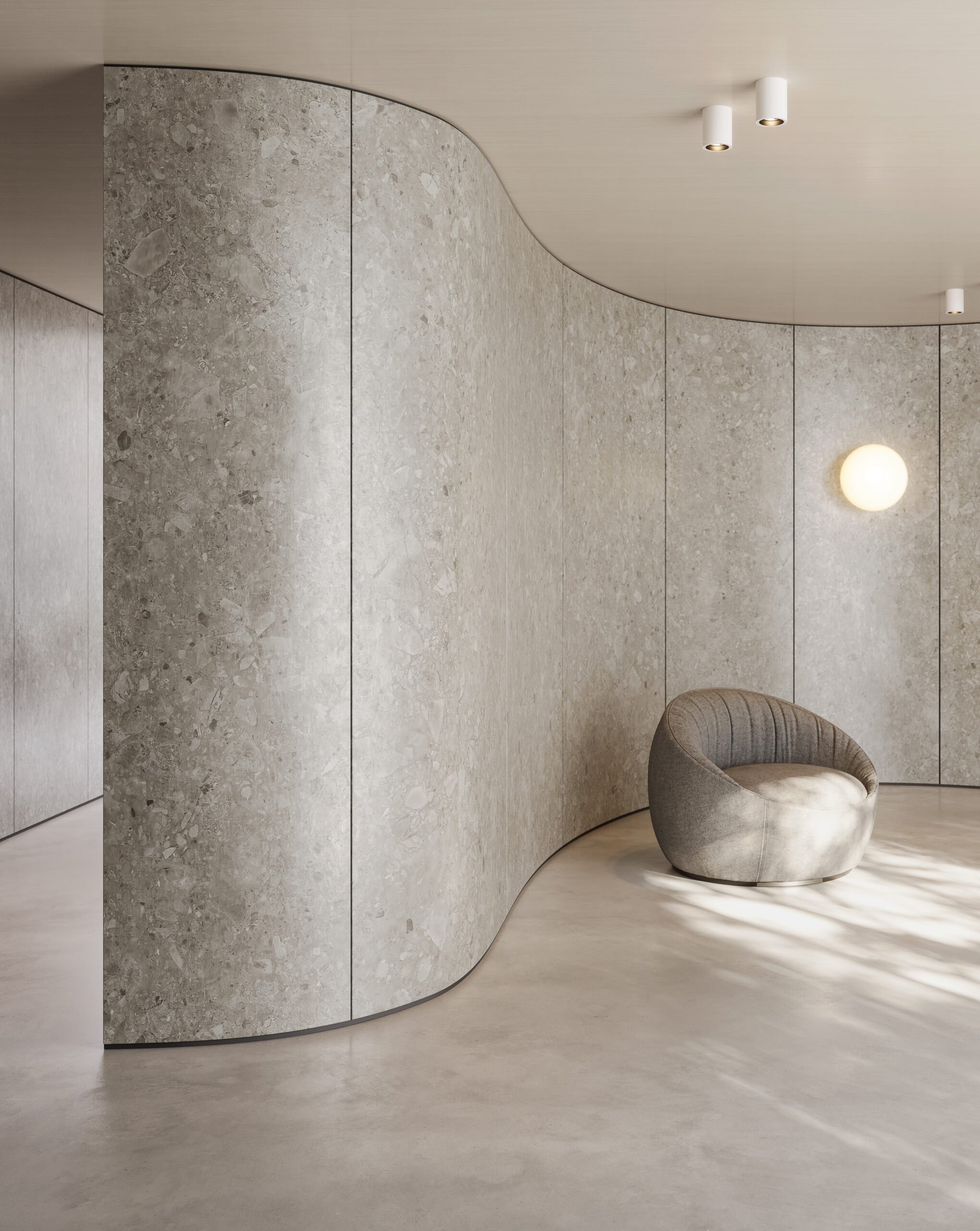 Moderne innendørsrom med kurvet vegg i lysegrå stein og en rund, komfortabel lenestol i grått stoff, opplyst av mykt belysning.