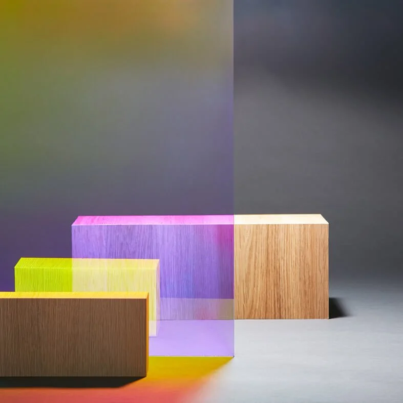 Fargede akryl- og treblokker på en grå bakgrunn, med refleksjoner og skygger.