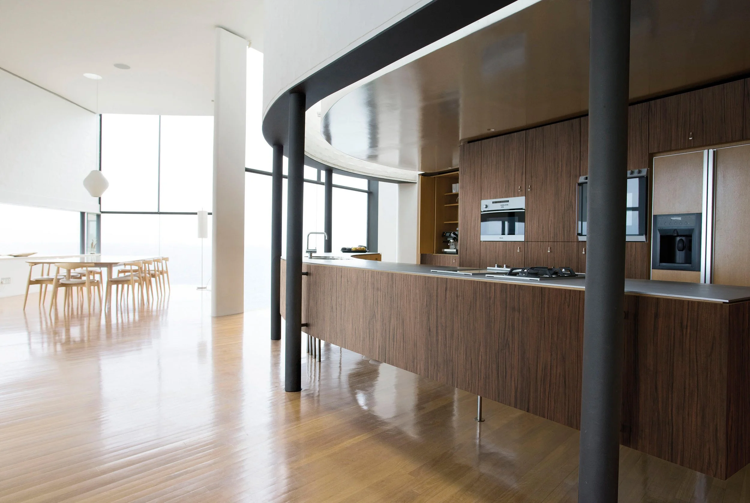 Moderne kjøkken med trehvite fronter, innebygd ovn og mikrobølgeovn, åpent til spisestue med store vinduer.