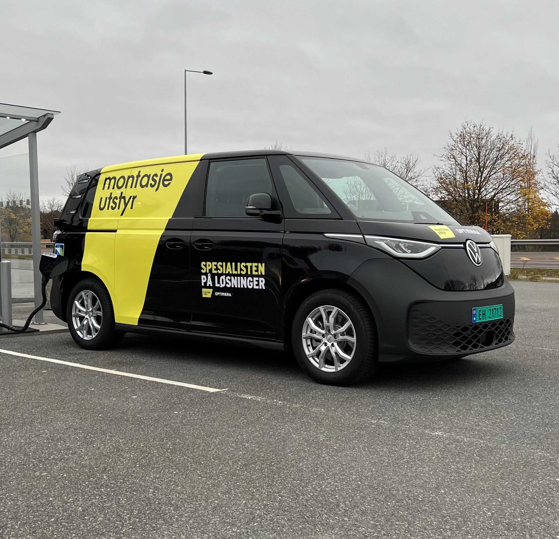 En svart elektrisk varebil som er ladet på en ladeplass, med reklame for Montasje Utstyr og løsning.