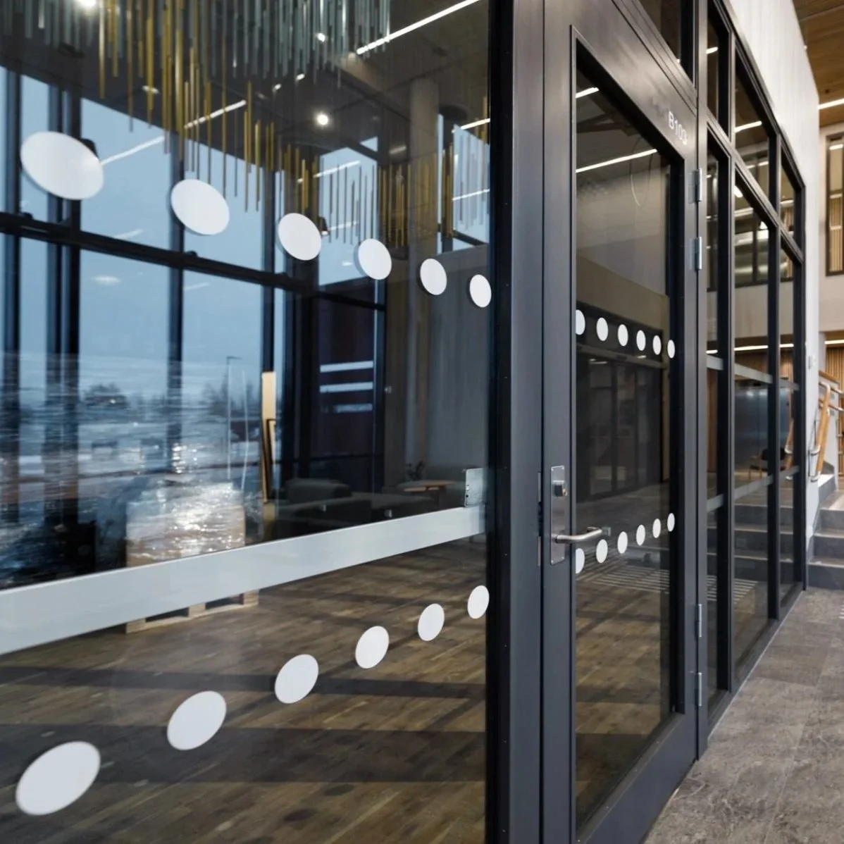 Innendørs kontorlokale med glass vegg og dør, dekorativ hvit prikkdekorasjon på glasset, tregulv og moderne belysning.