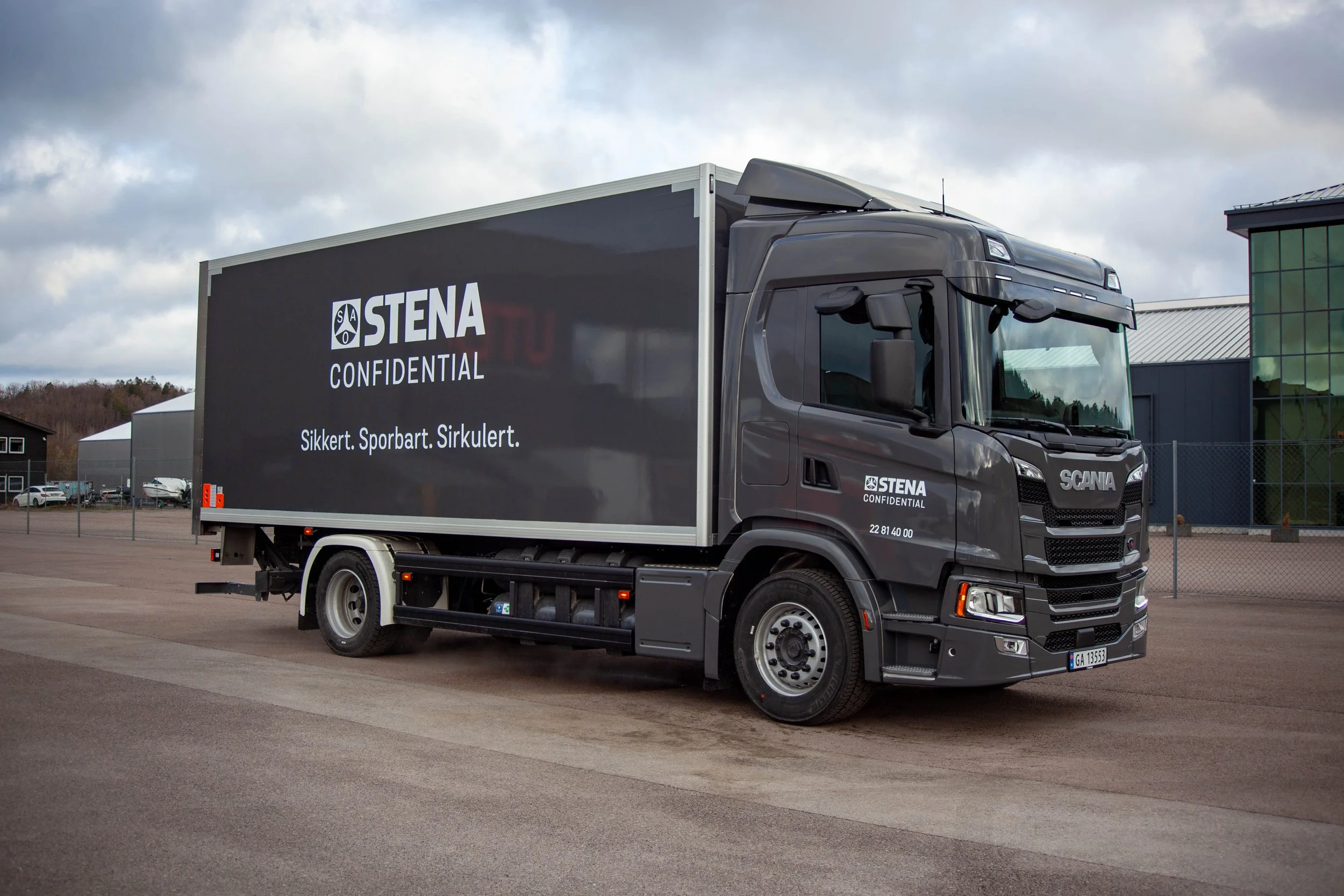 En svart lastebil med logoen til Stena Confidential, parkert på en tom uteplass. Ved siden av en moderne bygning med glassfasade.
