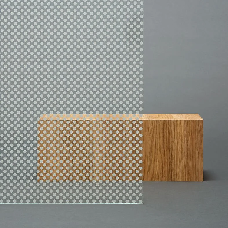 Et rektangulært stykke treverk plassert foran en grå bakgrunn, delvis dekket av en transparent, prikkete plastfolie.