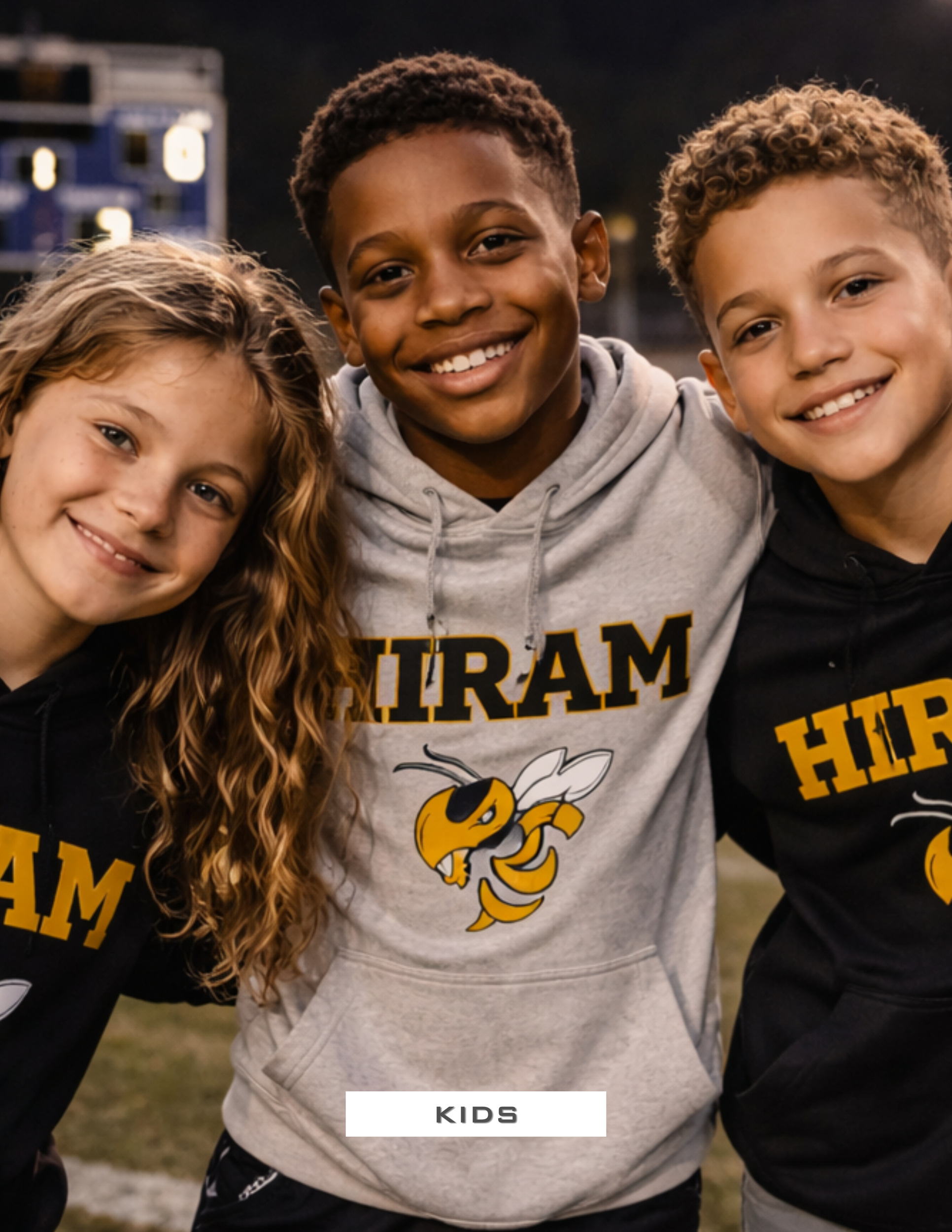 Three kids smiling and posing closely together outdoors, wearing hoodies with a yellow and black hornet mascot and the word 'HIRAM' printed on them.