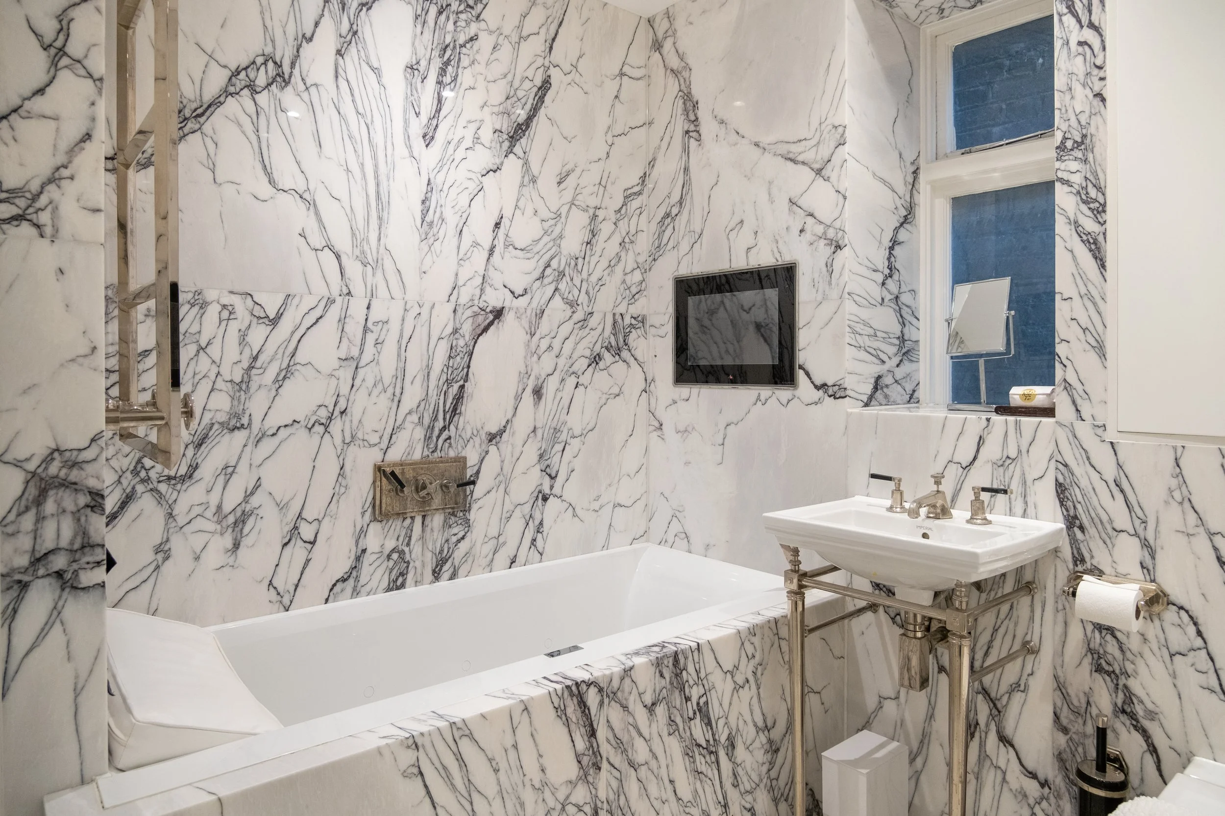 Luxury bathroom with dramatic white marble walls, freestanding bathtub, pedestal sink, and chrome fixtures