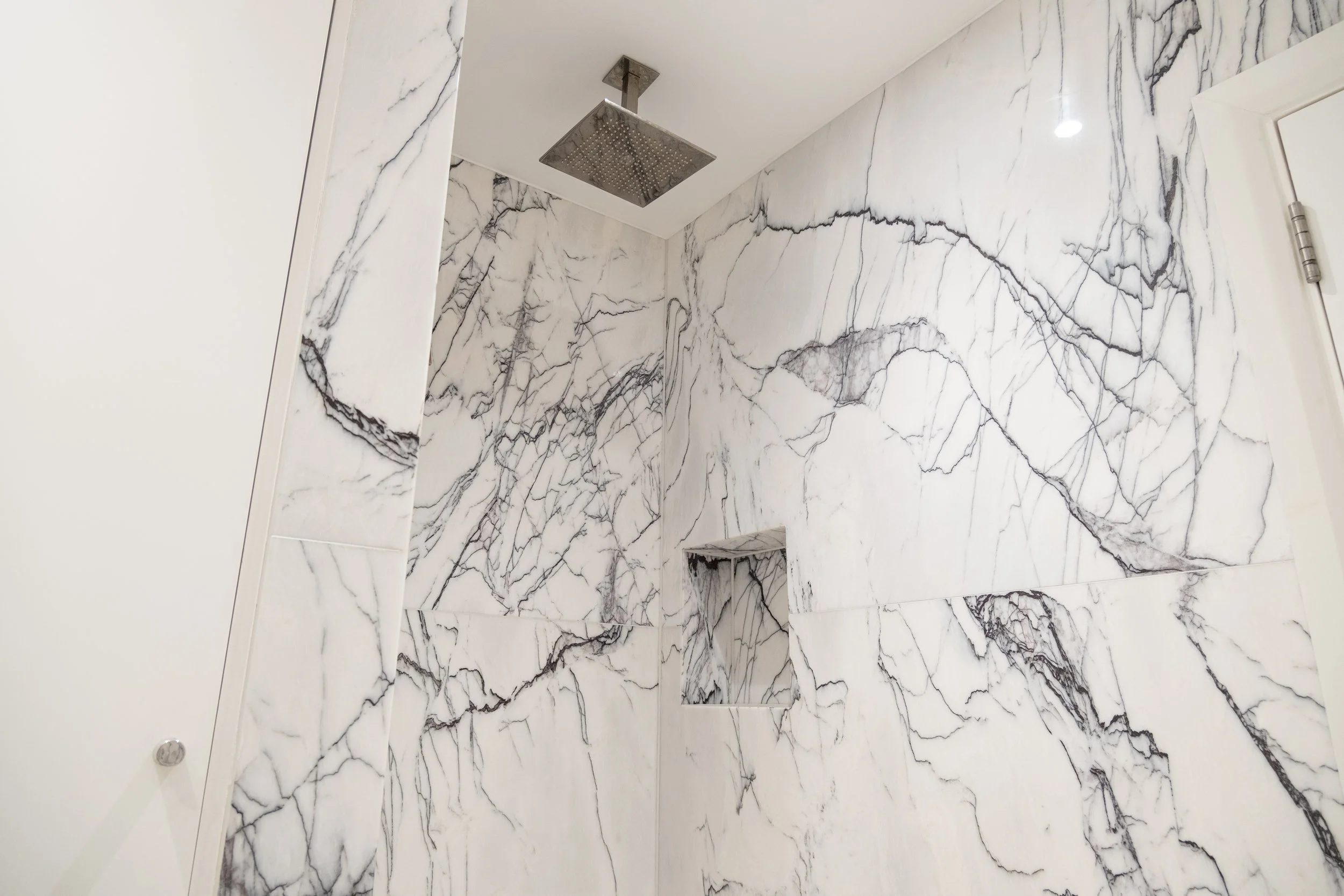 Luxurious walk-in shower with white marble-look walls, black veining, recessed niche, and square rainfall showerhead