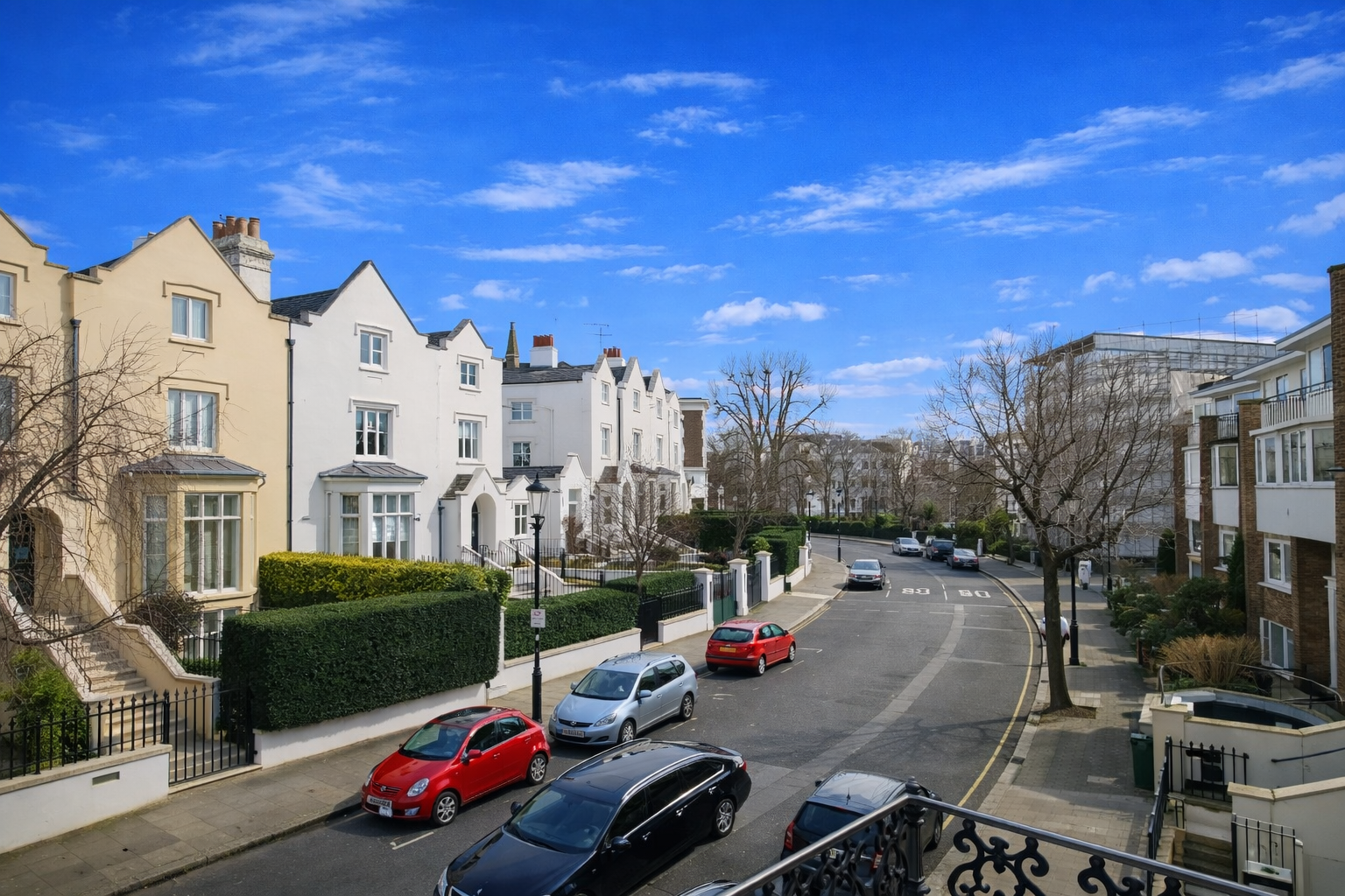 Residential London street with elegant townhouses, parked cars, leafless trees, and a bright blue sky