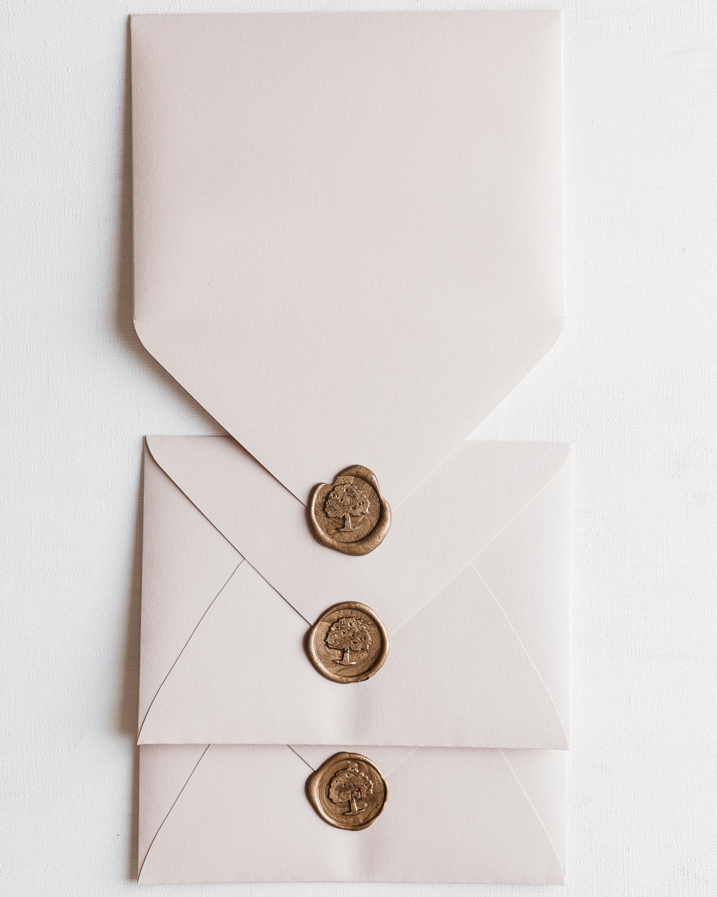 Three white envelopes with gold wax seals featuring a tree design, arranged vertically on a white background.