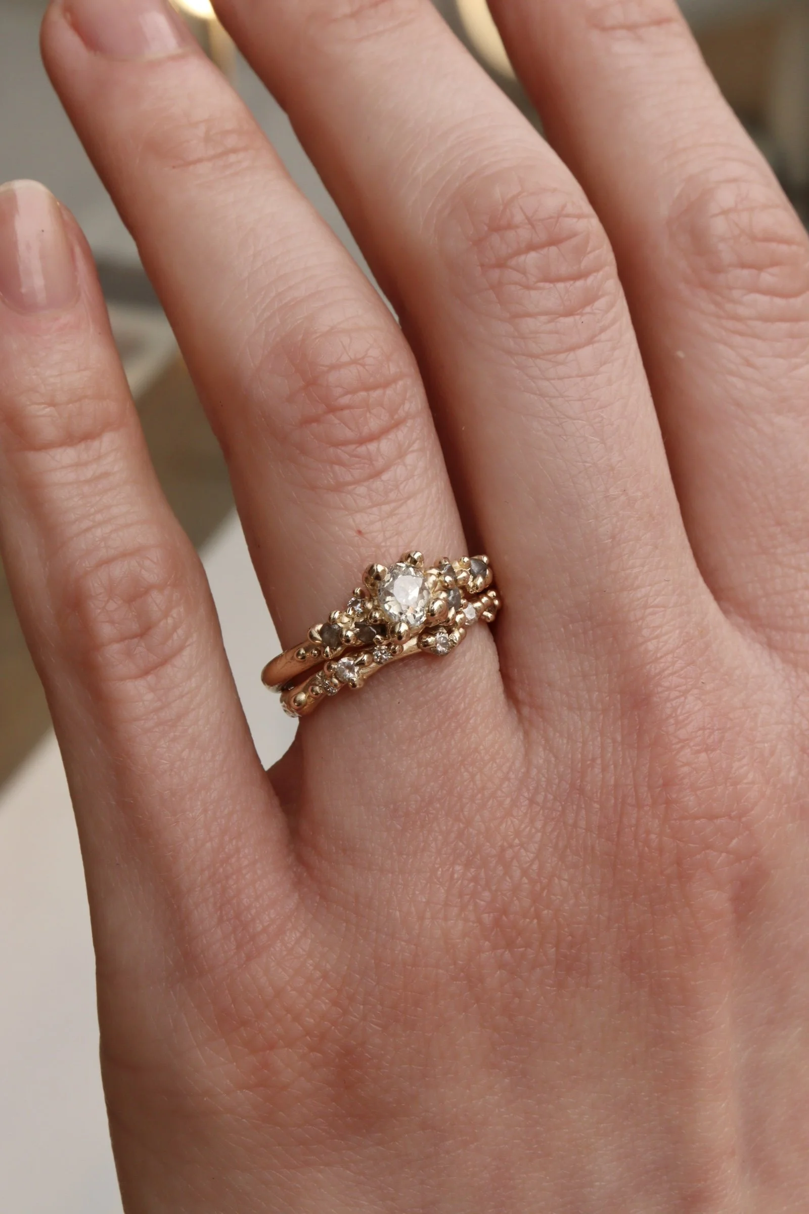 Close-up of a woman's hand with a gold ring featuring a prominent central diamond and smaller surrounding diamonds on her ring finger.