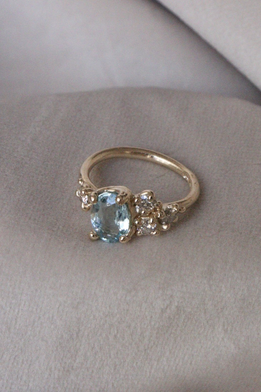 A gold ring with an oval-cut blue gemstone and small clear diamonds on a gray surface.