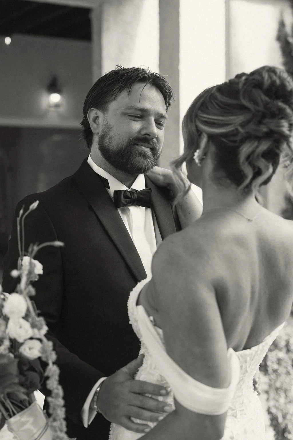 A wedding couple sharing a moment, the groom in a tuxedo and bow tie, the bride in a strapless dress with curled hair and earrings, during their wedding dance.