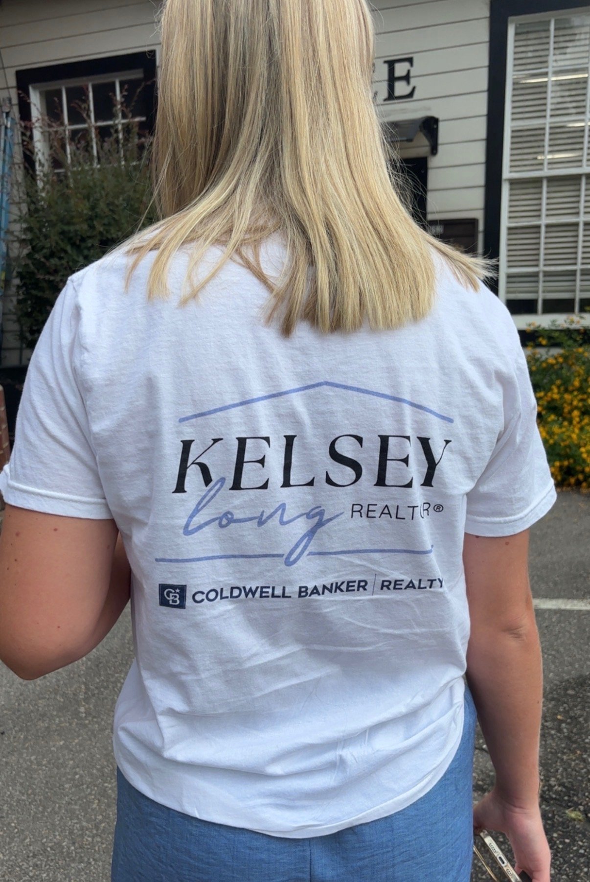 Woman wearing white t-shirt with Kelsey Long Realtor and Coldwell Banker Realty logo on the back