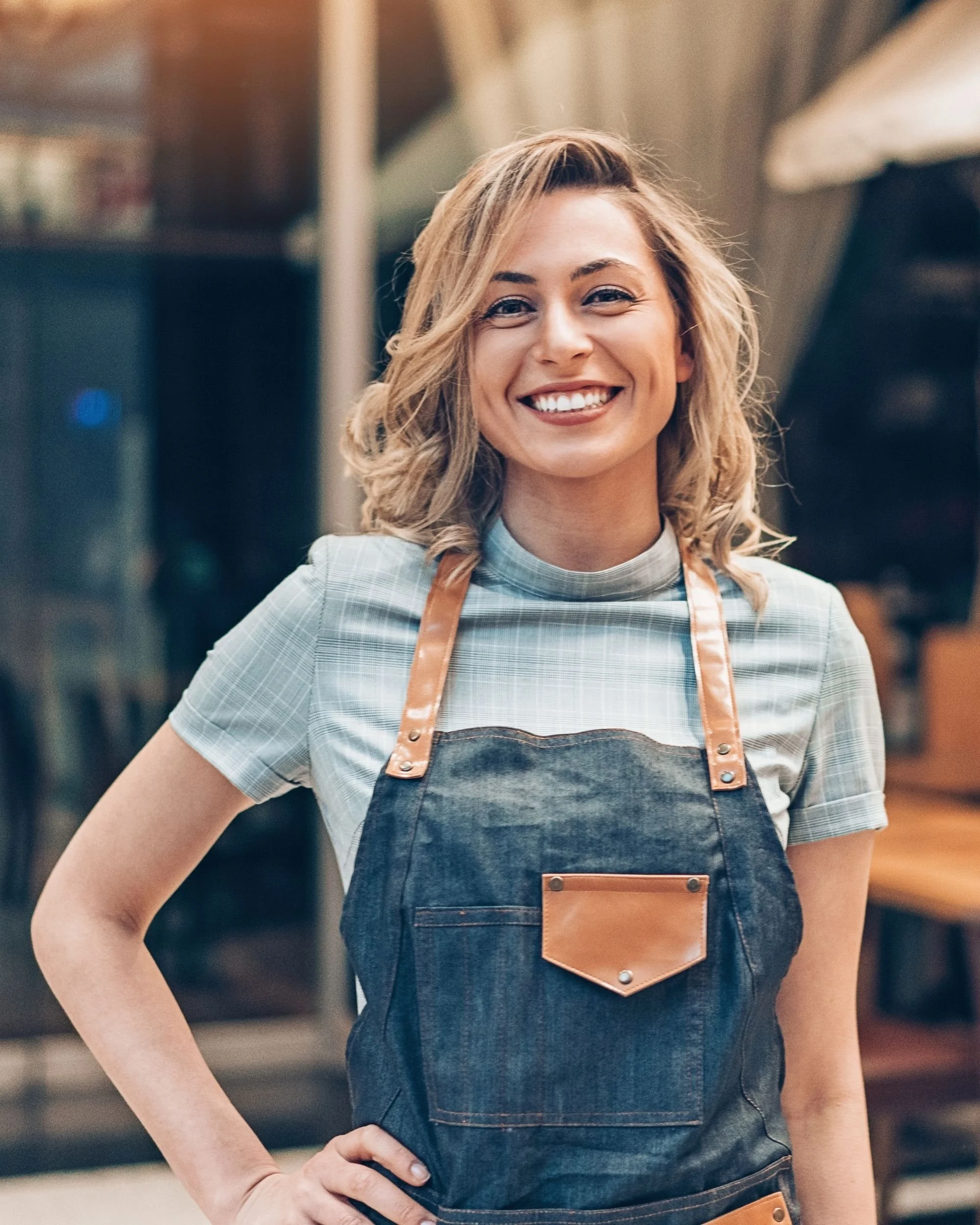Smiling small business owner wearing an apron standing in front of her storefront