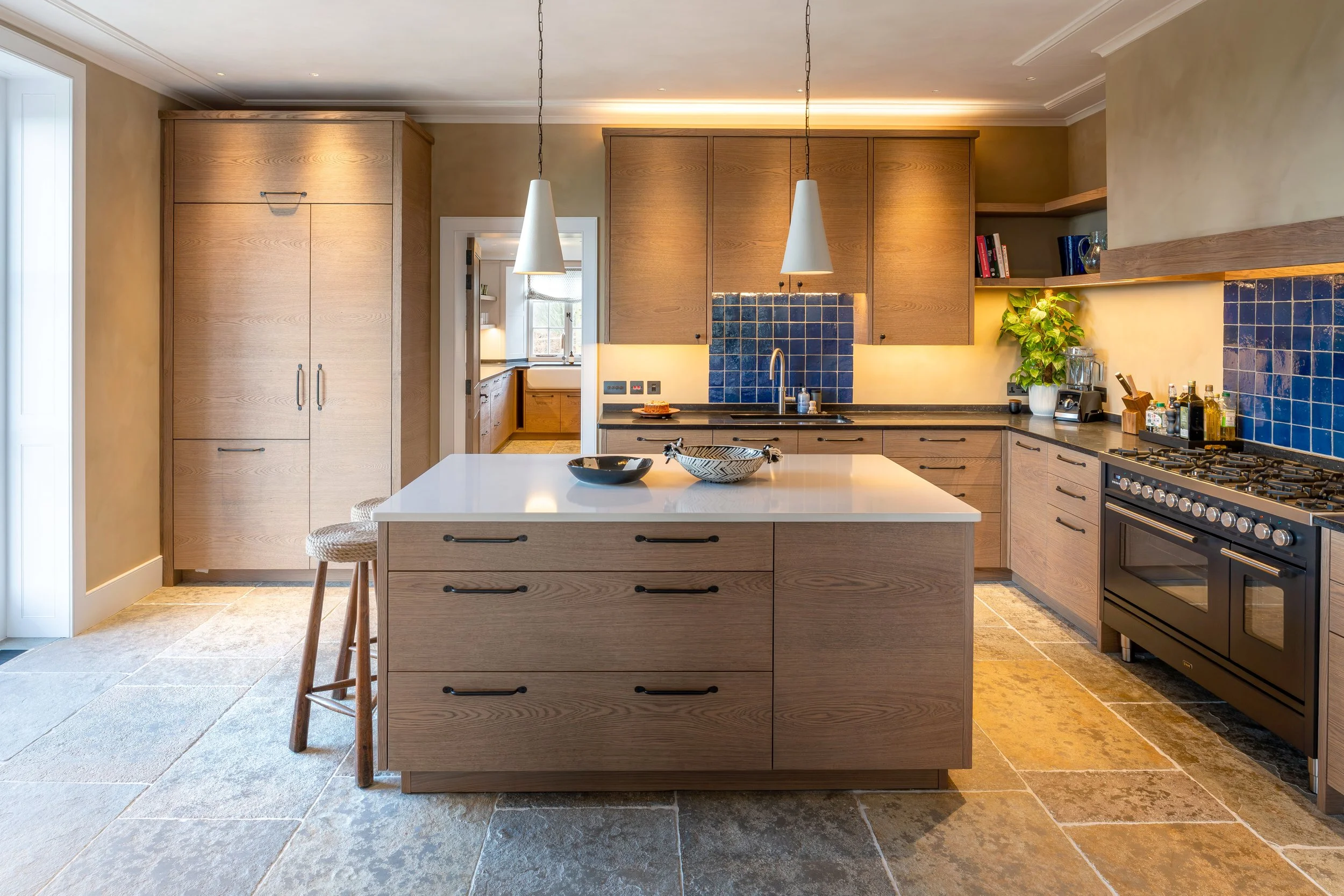 Modern kitchen with wooden cabinets, blue tiled backsplash, white island, and pendant lights.