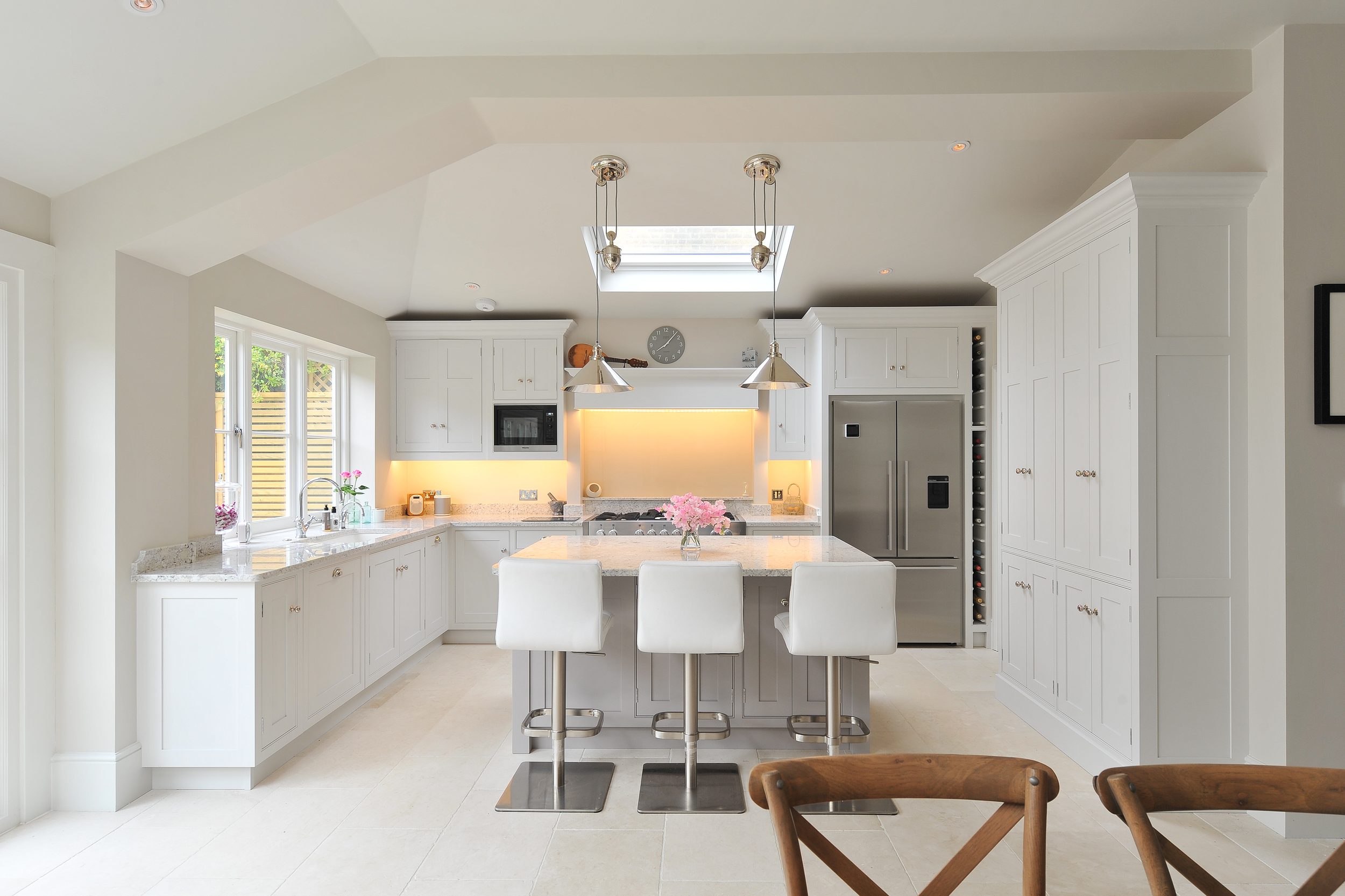 Bright modern kitchen with white cabinetry, island with flower arrangement, stainless steel appliances, and vaulted ceiling with skylight.