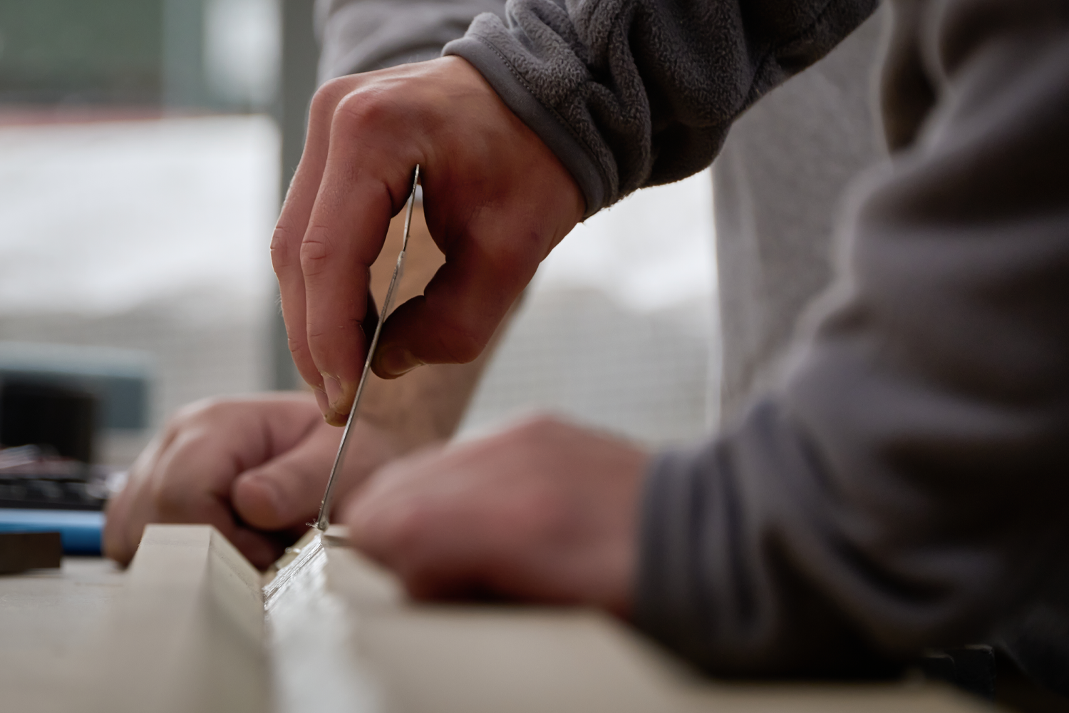 A person's hands working on a craft project, using a small metal tool on a light-colored wooden surface.