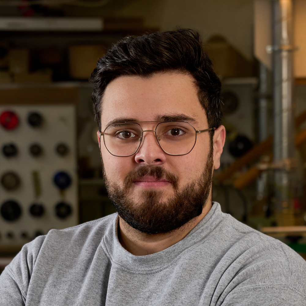Portrait of a man with glasses and a beard in a workshop or garage setting.