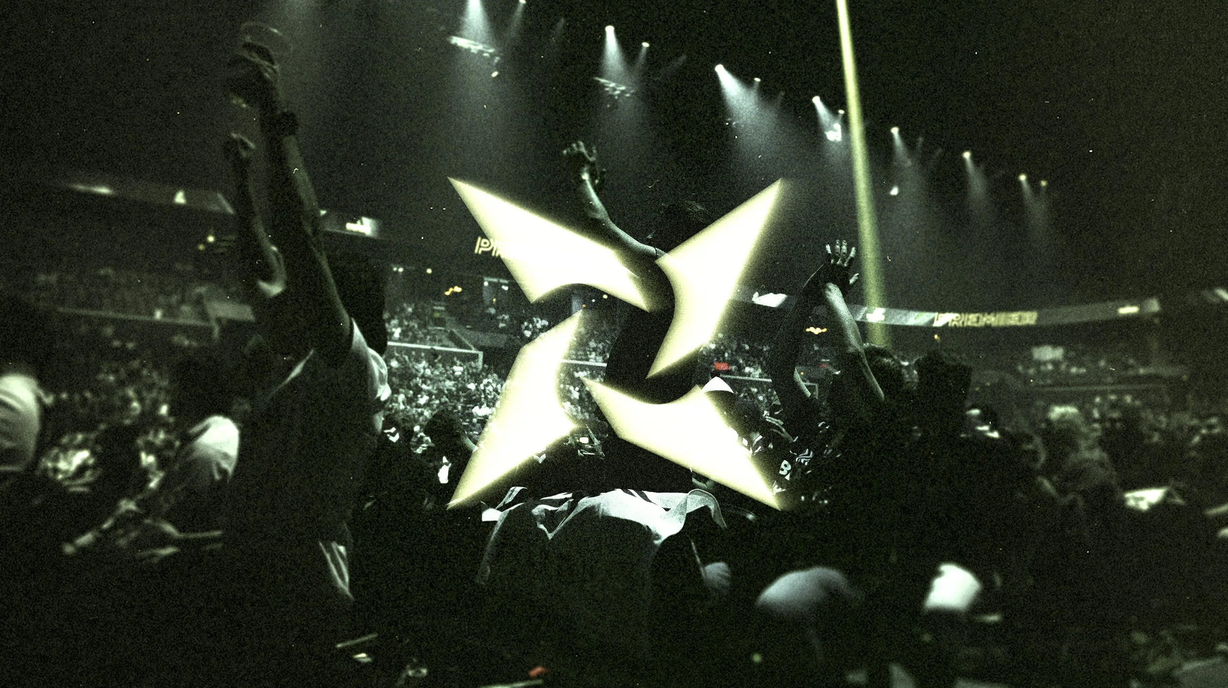 A crowd of people at a concert with a large illuminated star-shaped object in the foreground and stage lights above.