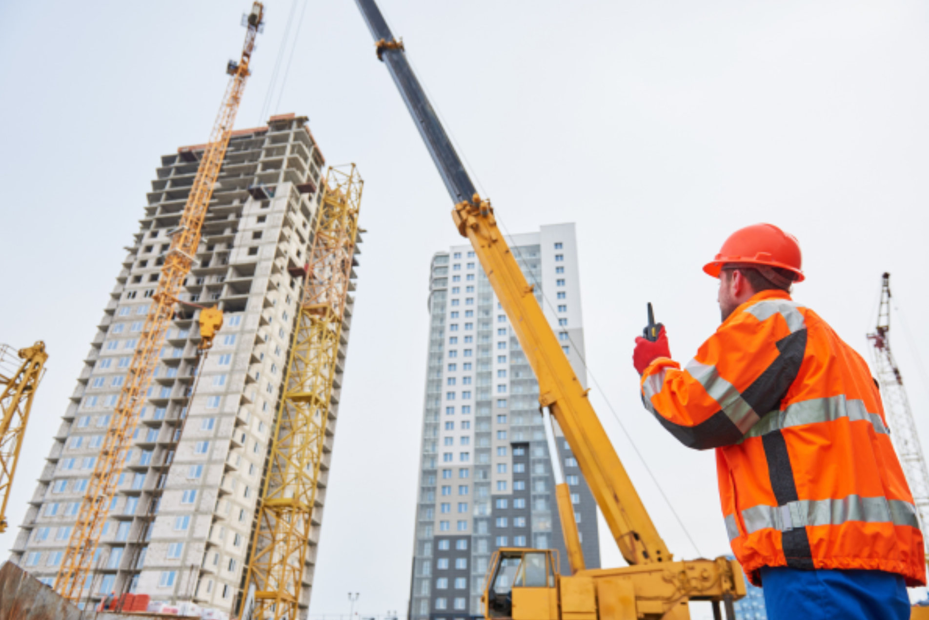 Site manager wearing PPE inspecting a construction crane on an active building site.